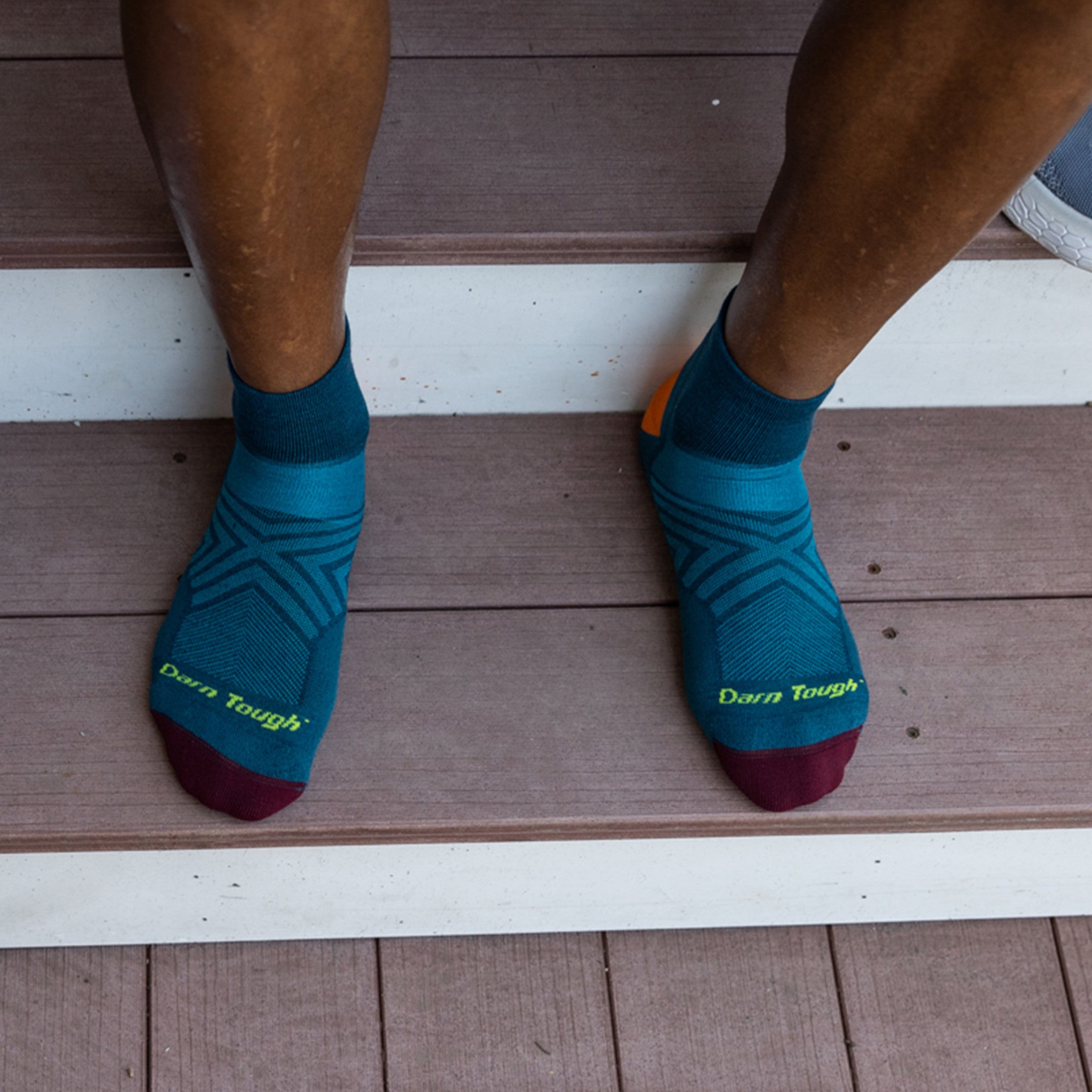 Overhead shot of model sitting on steps wearing the men's quarter running sock in dark teal