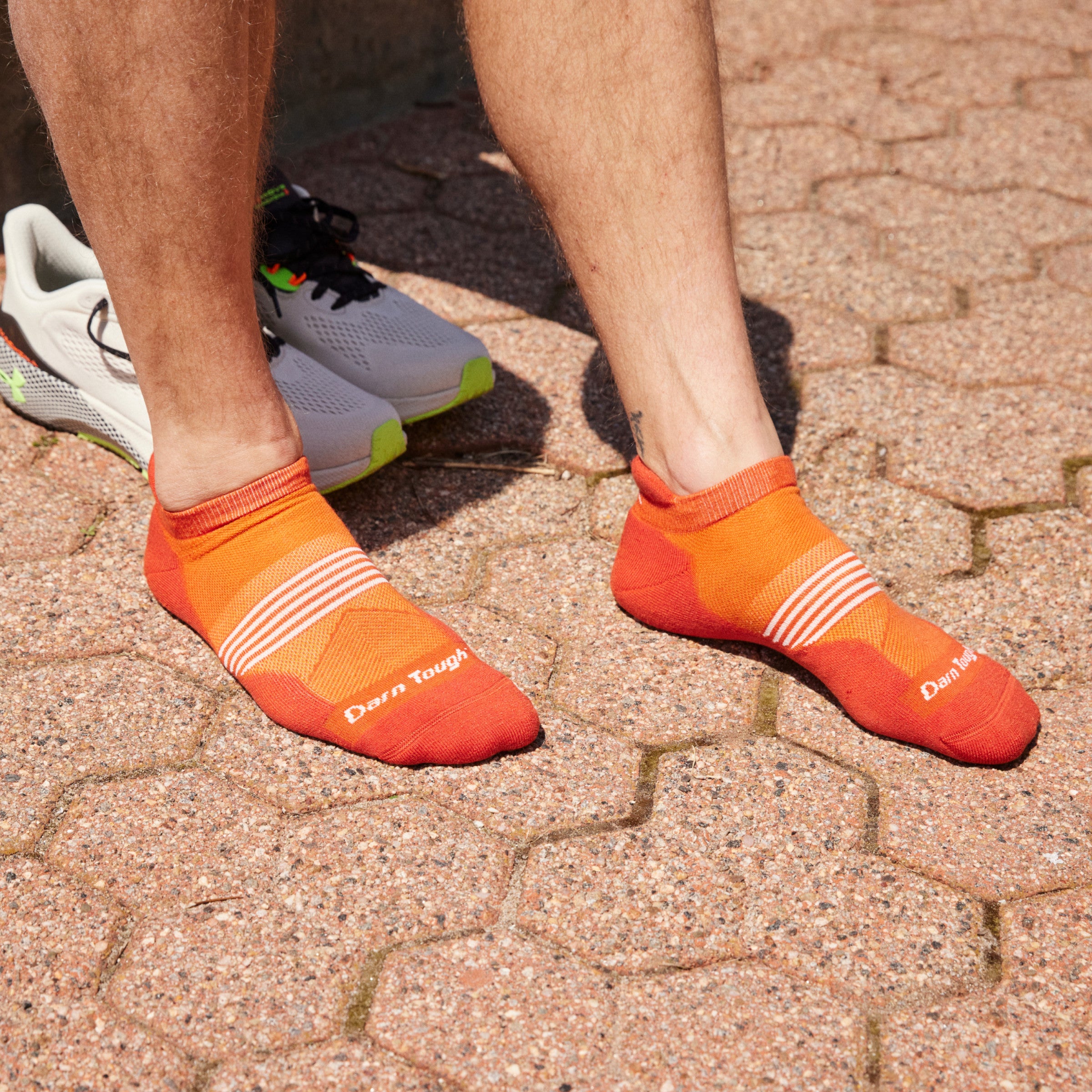 Close up shot of model wearing 1116 socks in Tiger colorway without shoes on and standing on light colored stone pavers