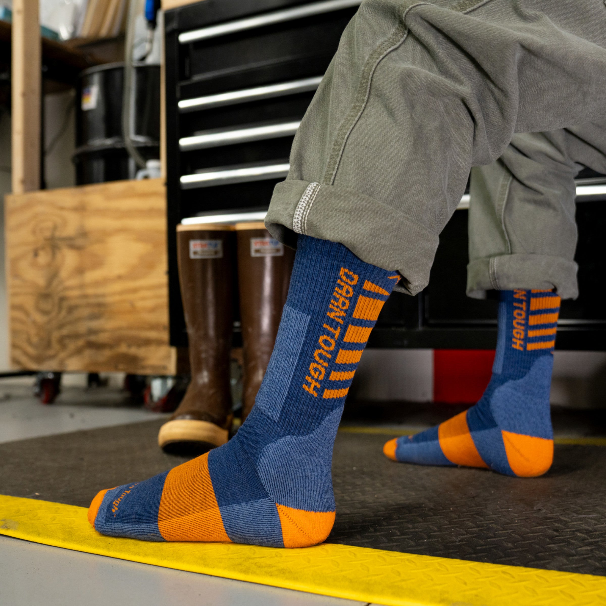 Models feet side image on a fatigue mat wearing the 2207 Backbone Midweight Boot sock in Indigo