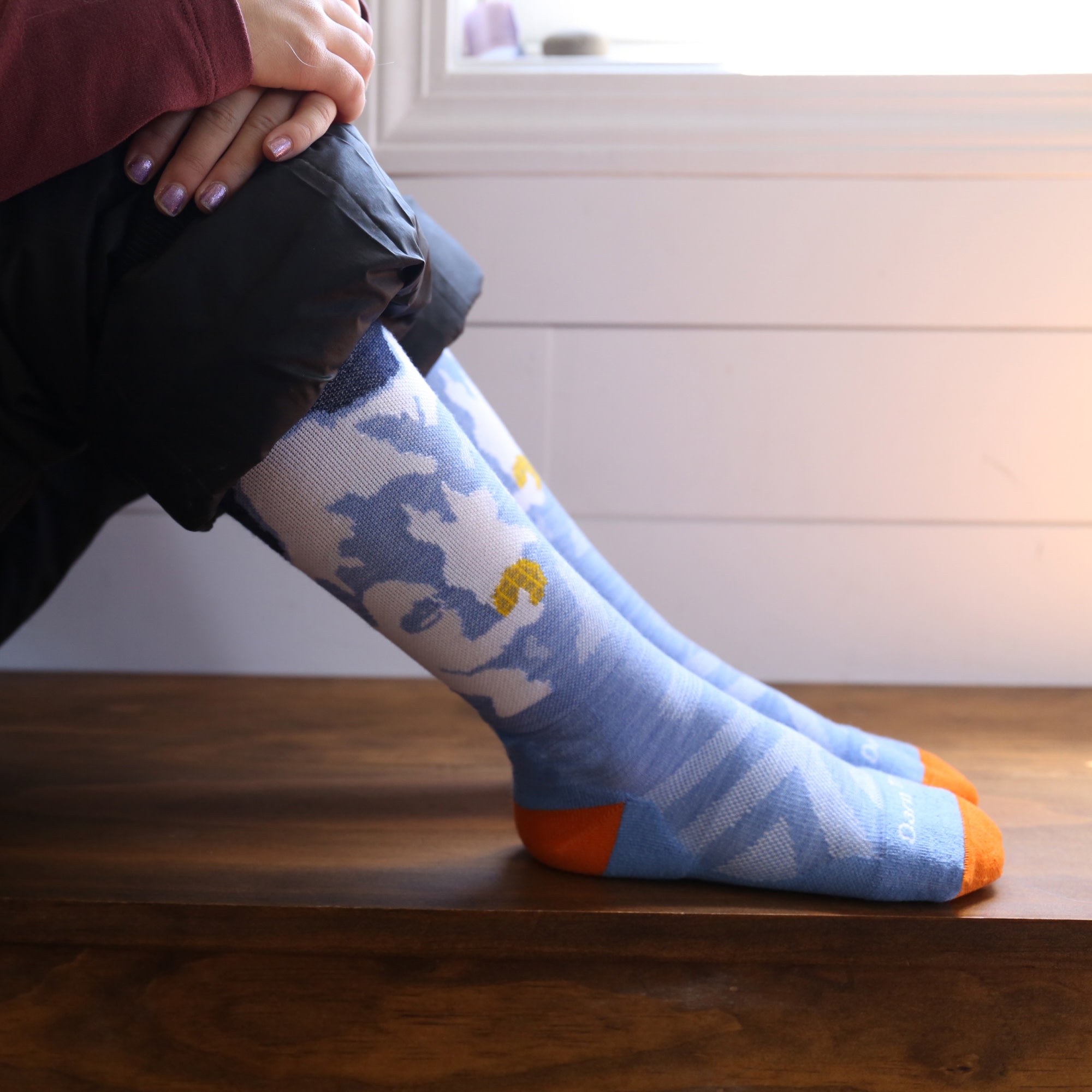 models feet up on a bench wearing the little yeti over the calf ski and snowboard sock in midnight colorway