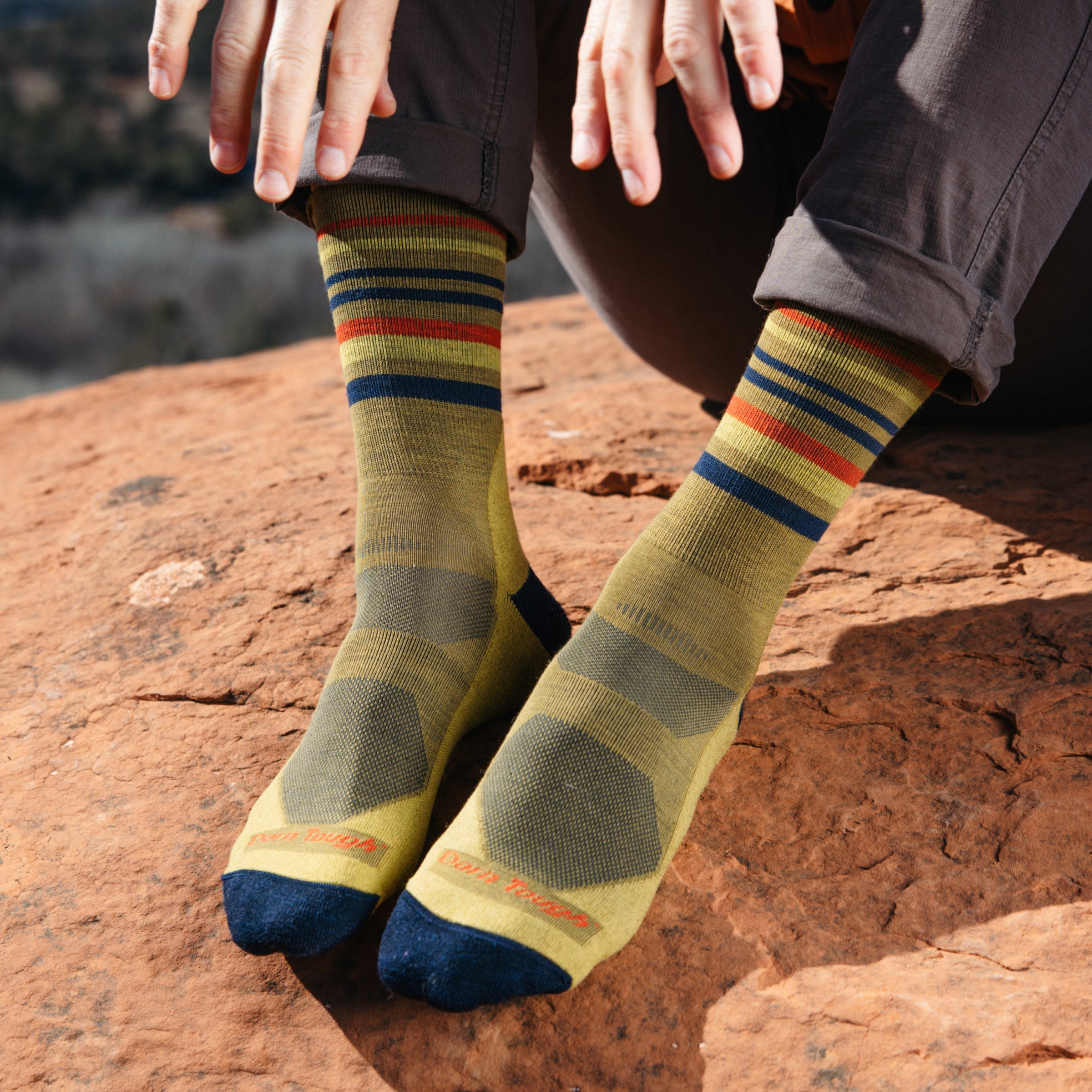 Model wearing 5012 socks in Sandstone colorway without shoes against red desert rock