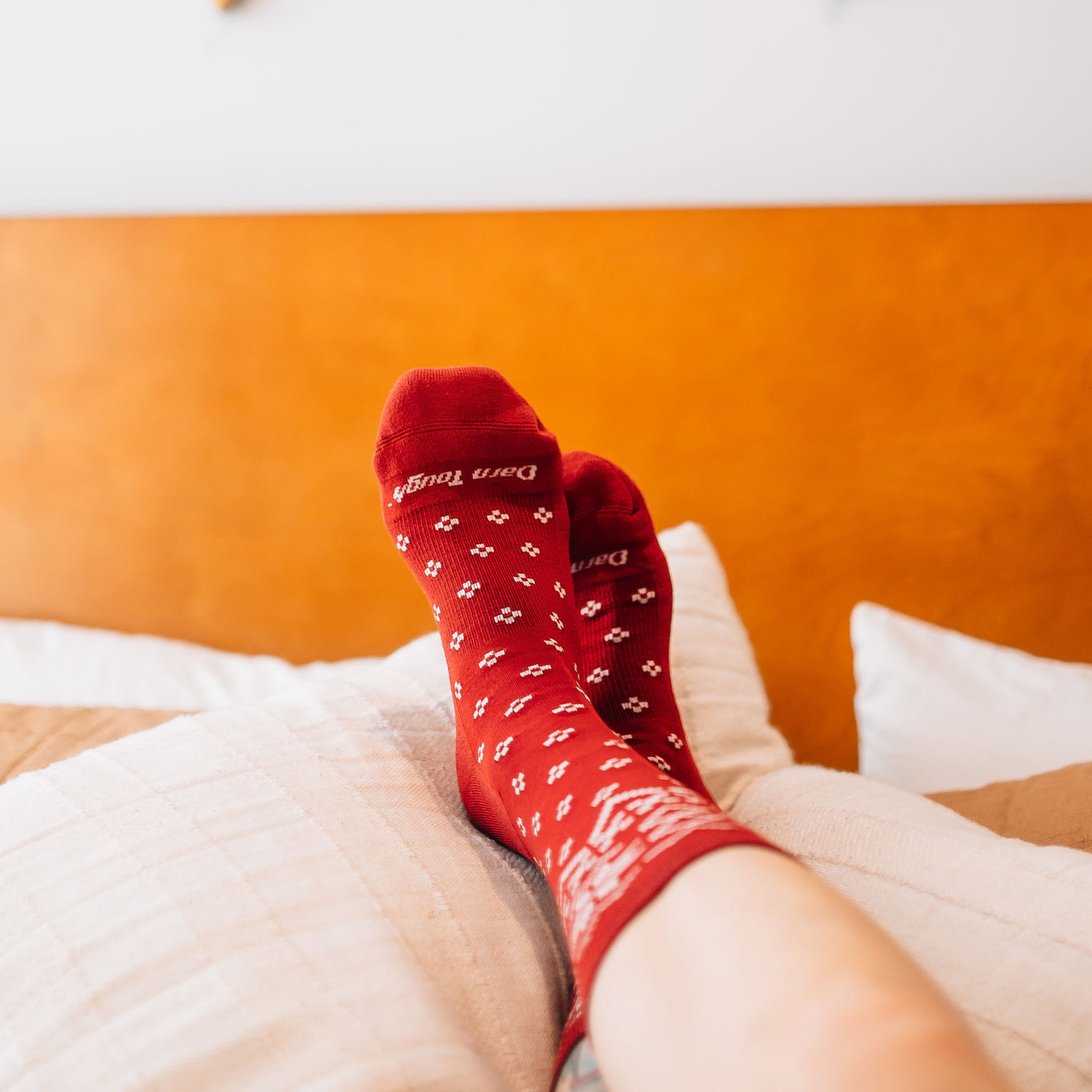 Model laying in bed with feet on top of pillows wearing the Women's Shetland Crew Lifestyle Sock in the cranberry color