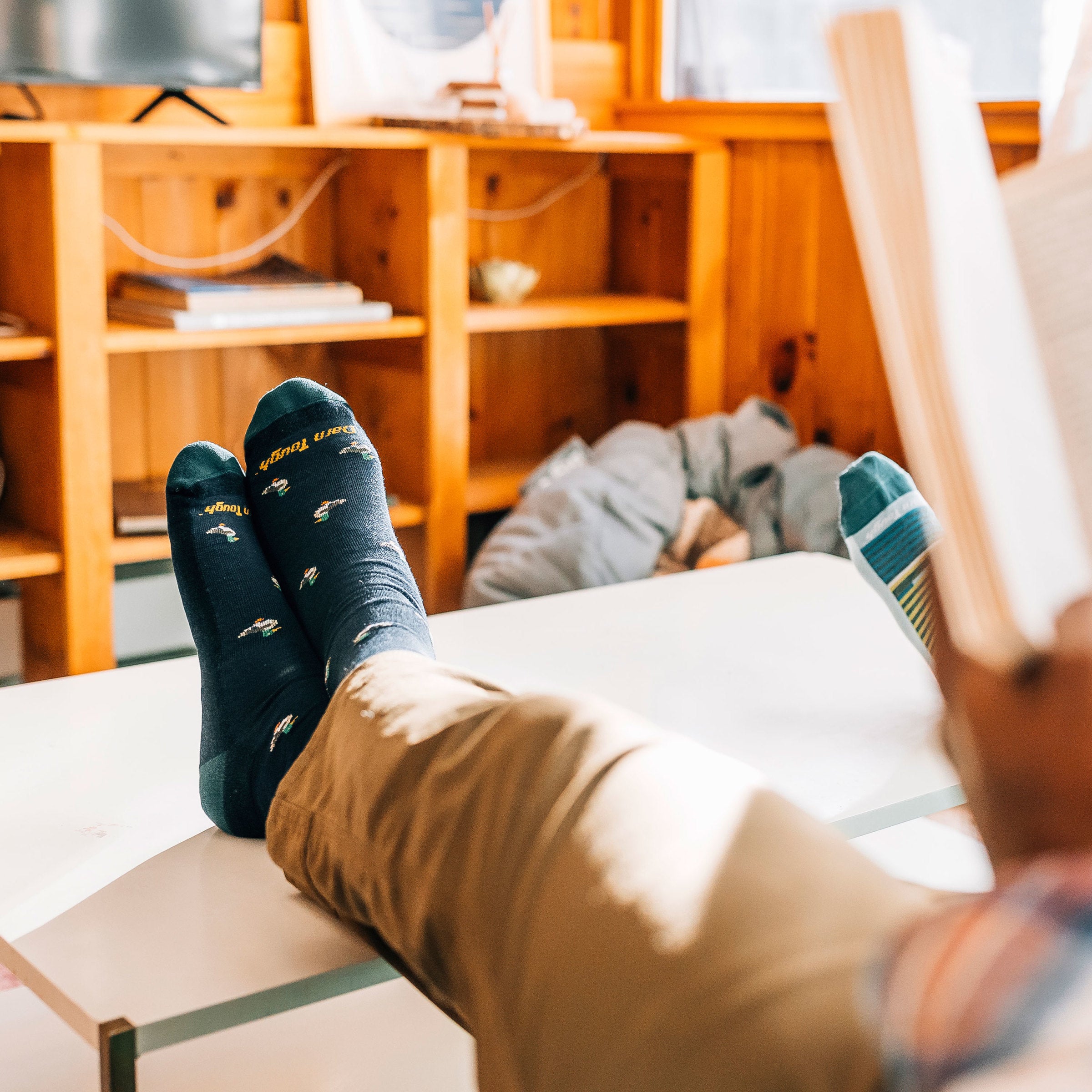 Shot of model laying down and reading with his feet up wearing men's duck duck moosee crew lifestyle sock in navy