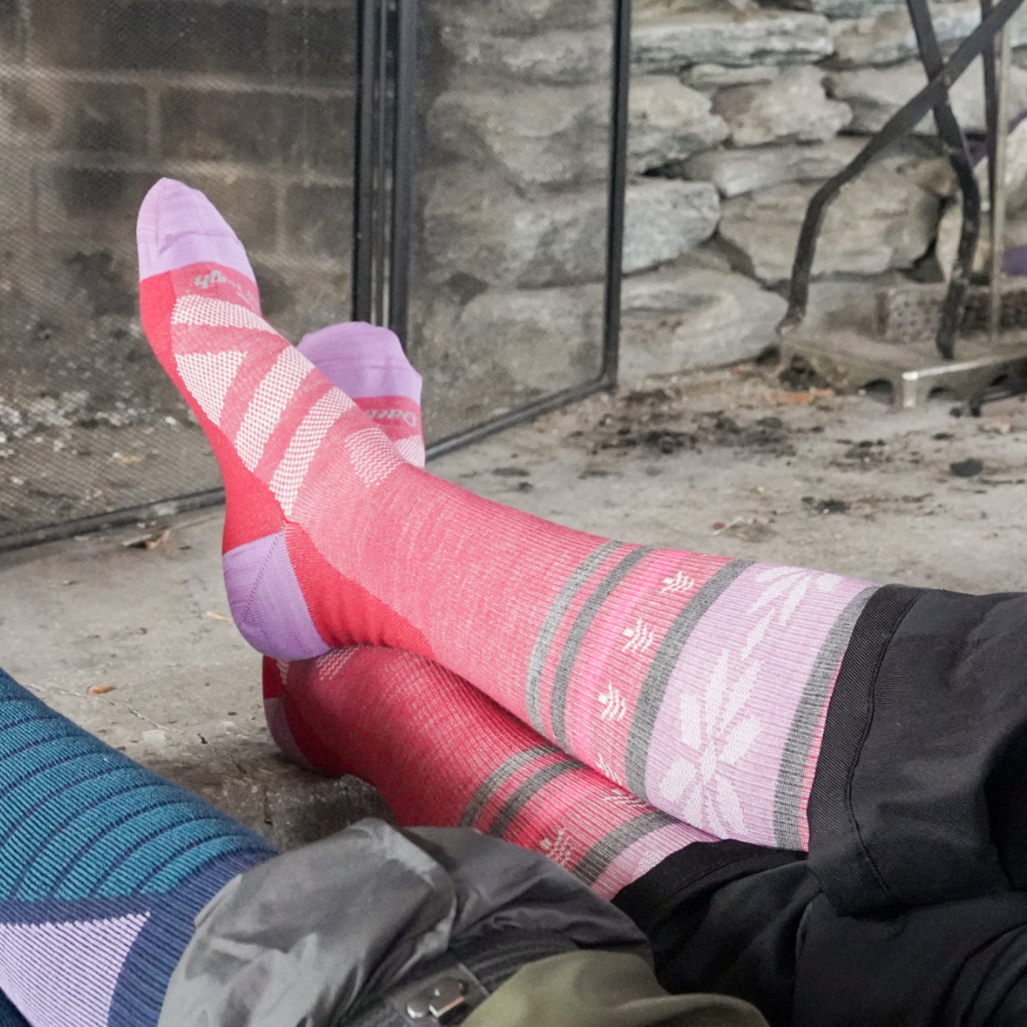 models feet up on a fireplace wearing the 8021 alpine over the calf ski and snowboard sock in cranberry