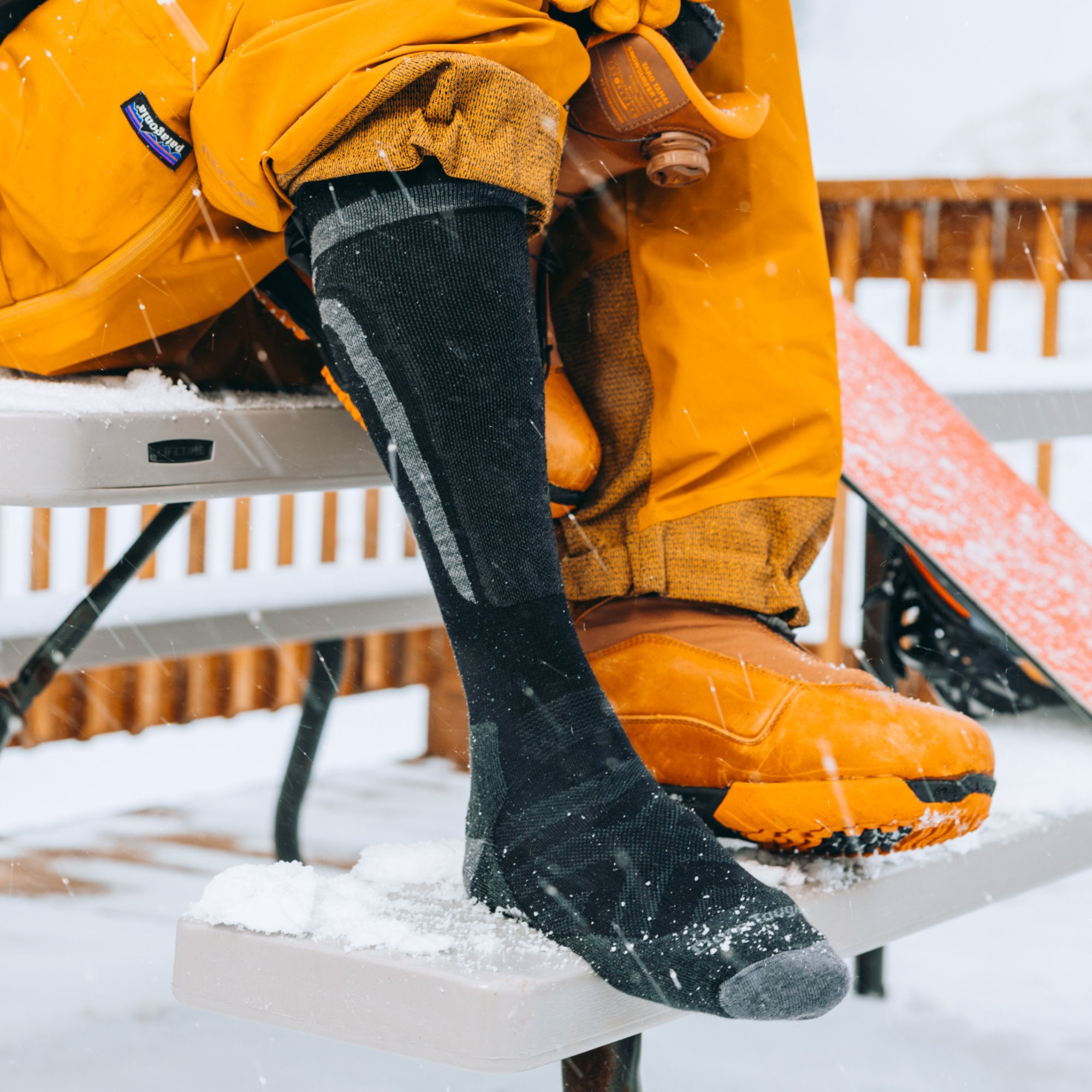 model sitting on picnic table wearing the 8053 edge over the calf ski and snowboard sock in black colorway