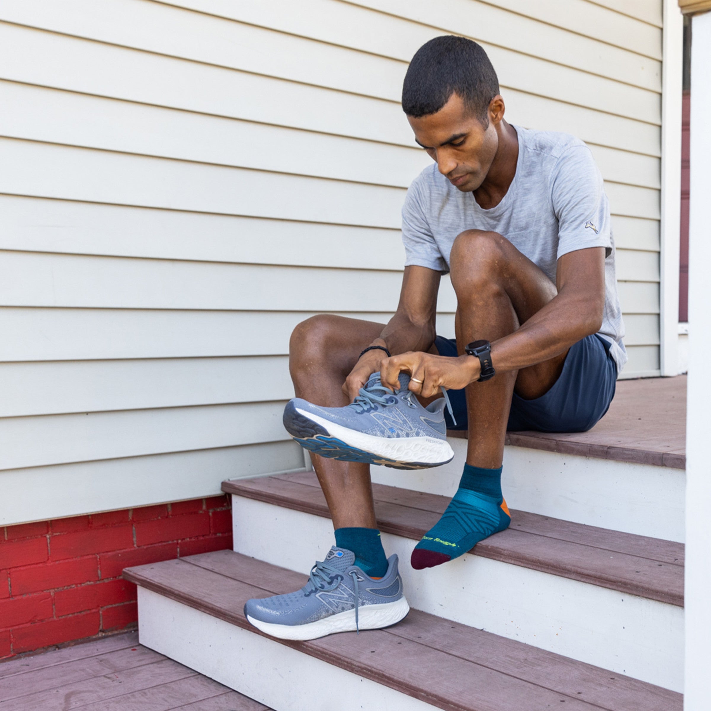 Full body shot of model sitting on steps putting on his shoes wearing the men's quarter running sock in dark teal