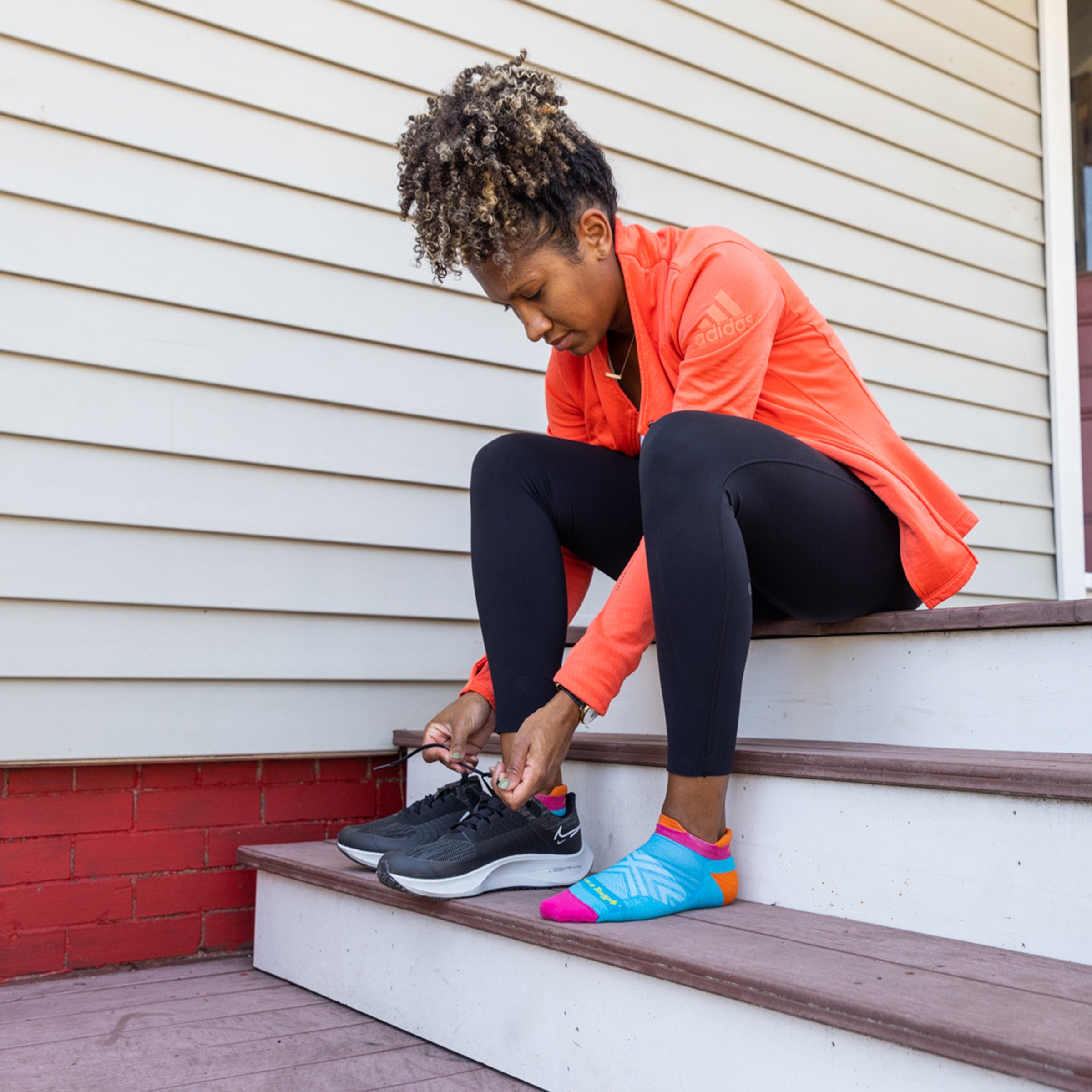 Shot of model sitting on steps putting on her shoes wearing the women's no show tab running sock in ocean blue