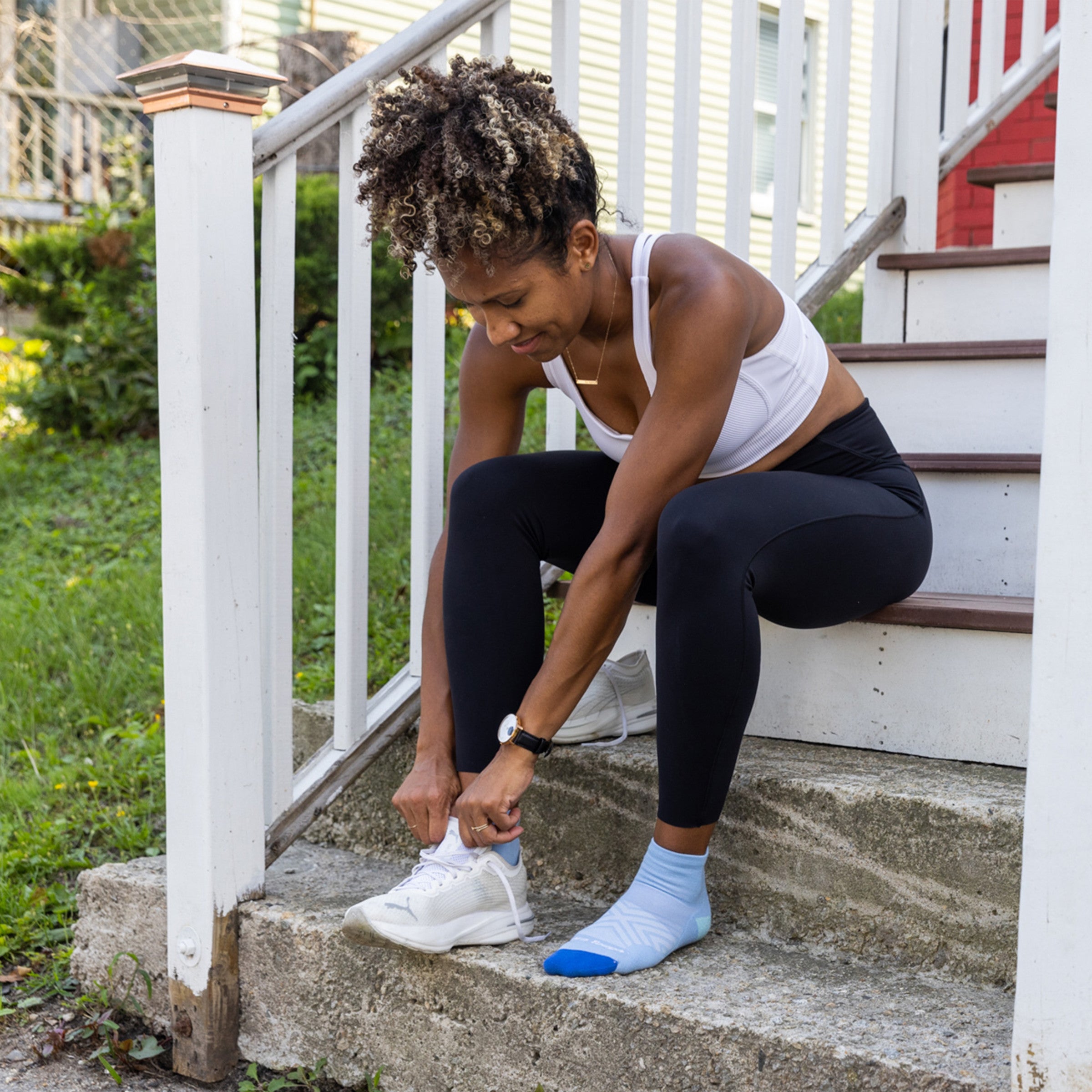 Full body shot of model sitting on steps putting on her sneakers wearing the women's quarter running sock in sky blue