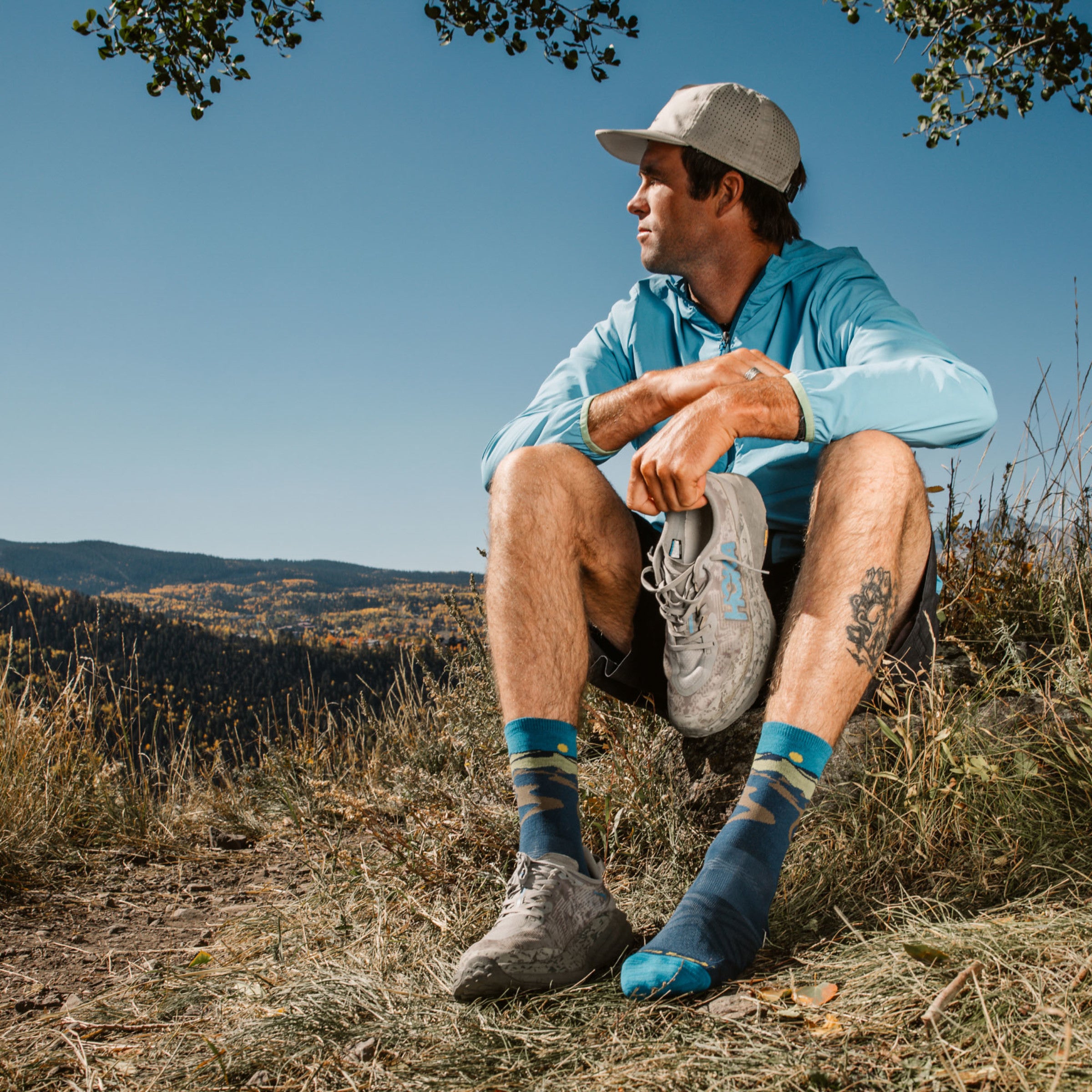 Model sitting in grass with one shoe off wearing the 1065 Ridge runner micro crew running sock in Midnight