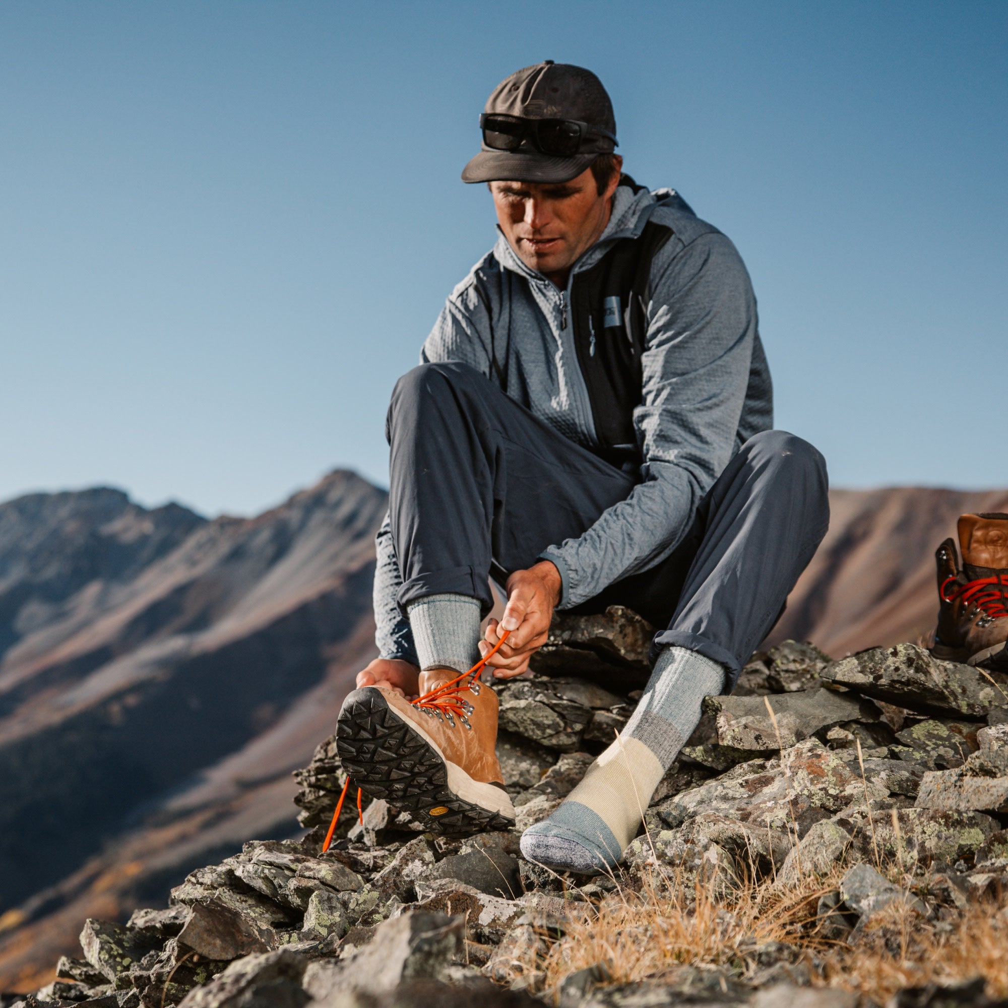 model sitting on top of mountain tying shoes wearing the 1053 micro crew mountaineering sock in geyser colorway