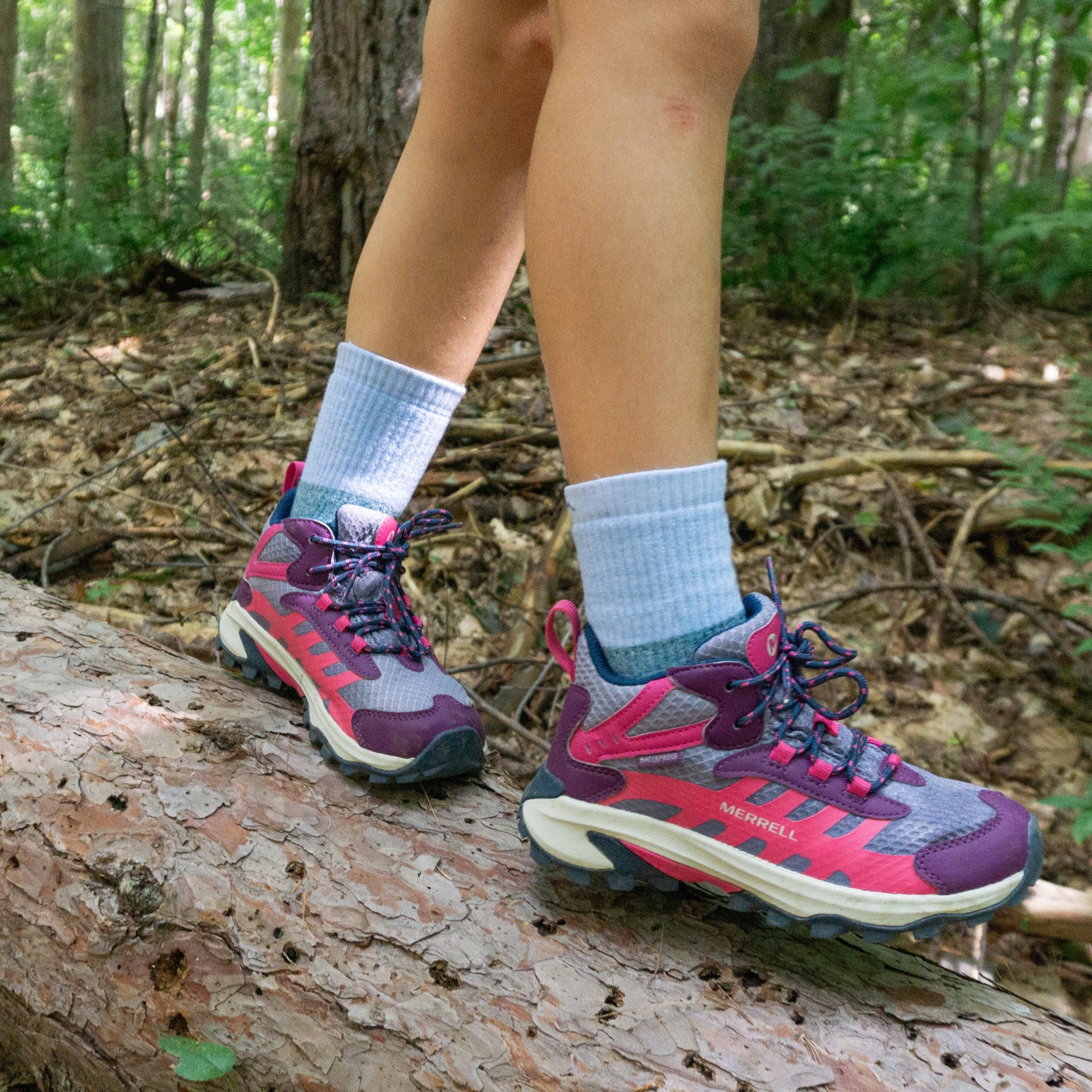 model walking across a log in sneakers wearing the 3045 hill topper micro crew sock in dragonfly blue colorway