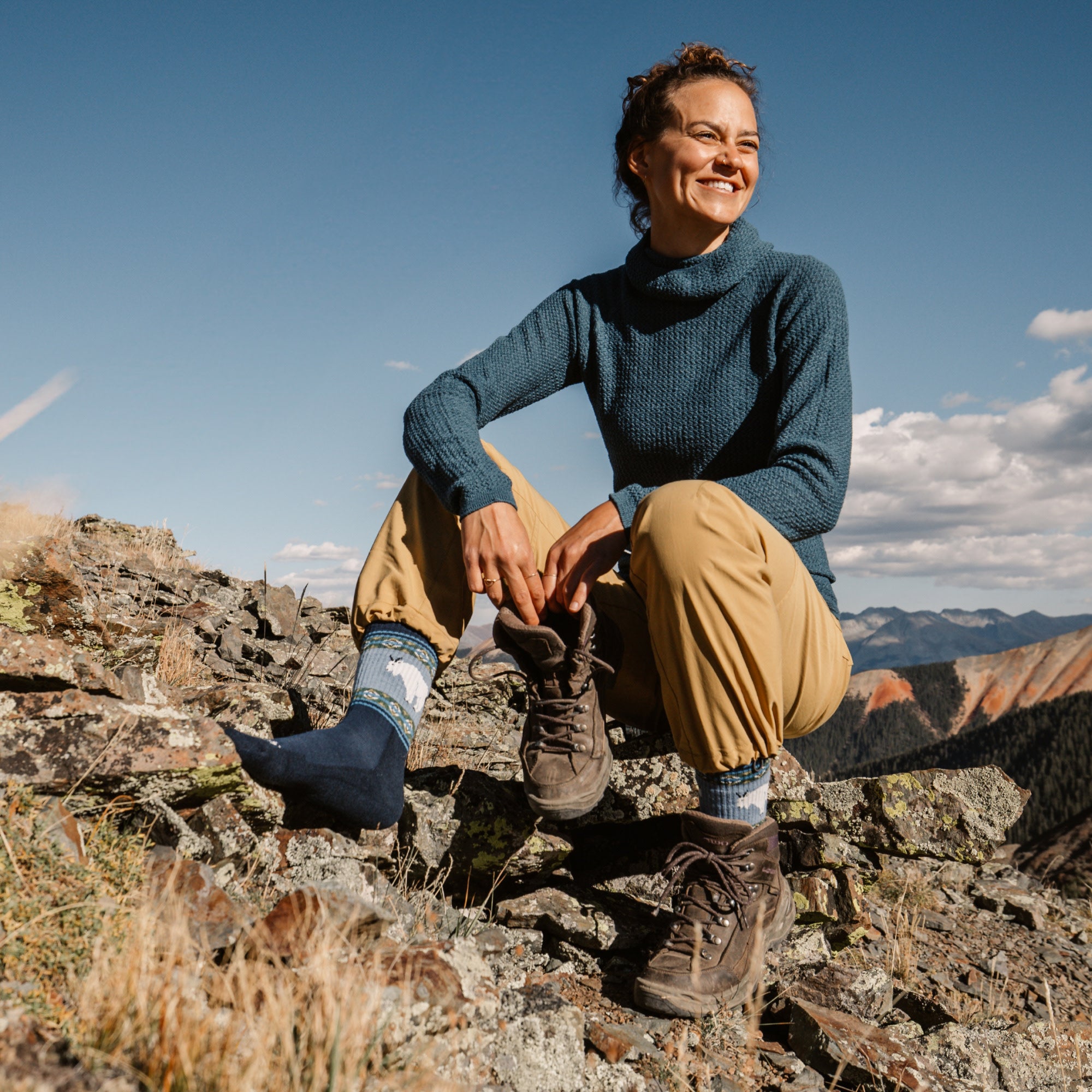 Model sitting on rocks putting shoes on wearing the 5017 vanna grizzle in goat blue