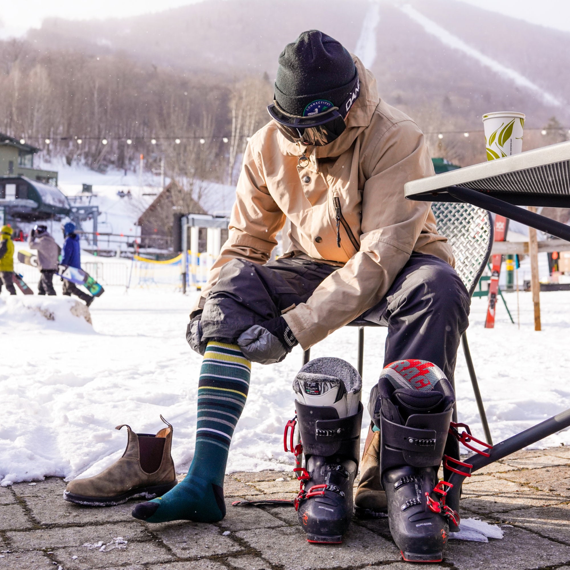 model sitting at able pulling on his 8017 snowpack over the calf ski and snowboard sock in pine colorway