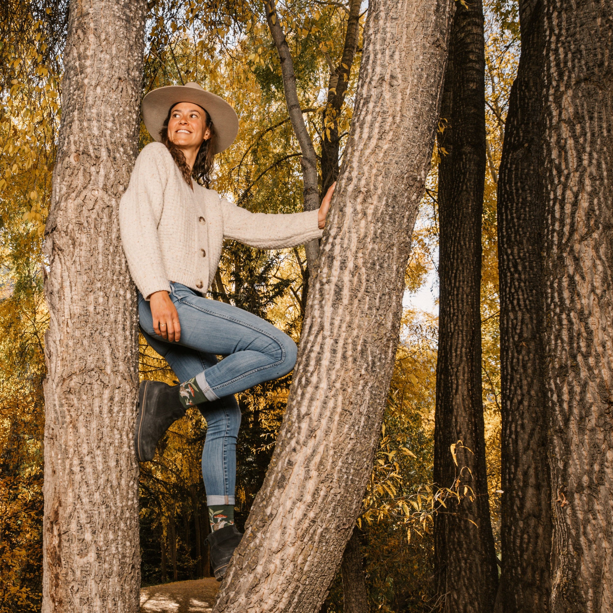 model standing between two trees with one leg up showing off her 6105 wildlife crew socks in hedgehog moss