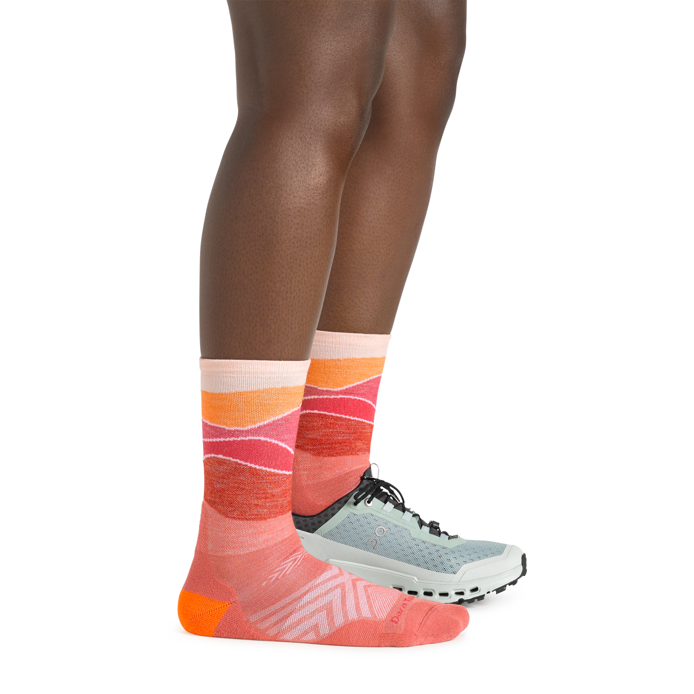 Side shot of model wearing the women's horizon micro crew running sock in canyon pink with a blue shoe on her left foot