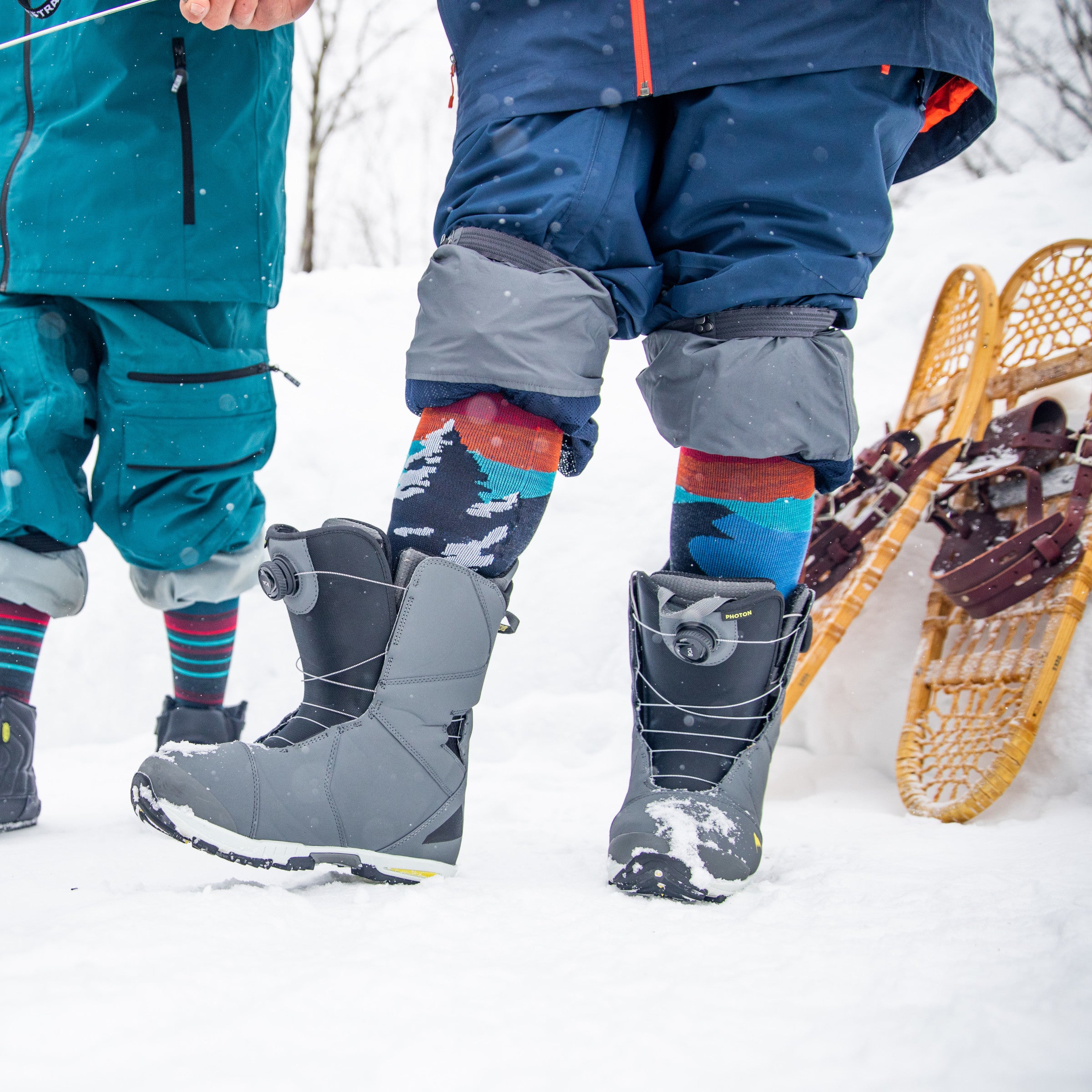 Close up shot of model in the snow wearing the men's solstice over-the-calf snow sock in charcoal with vintage snow shoes