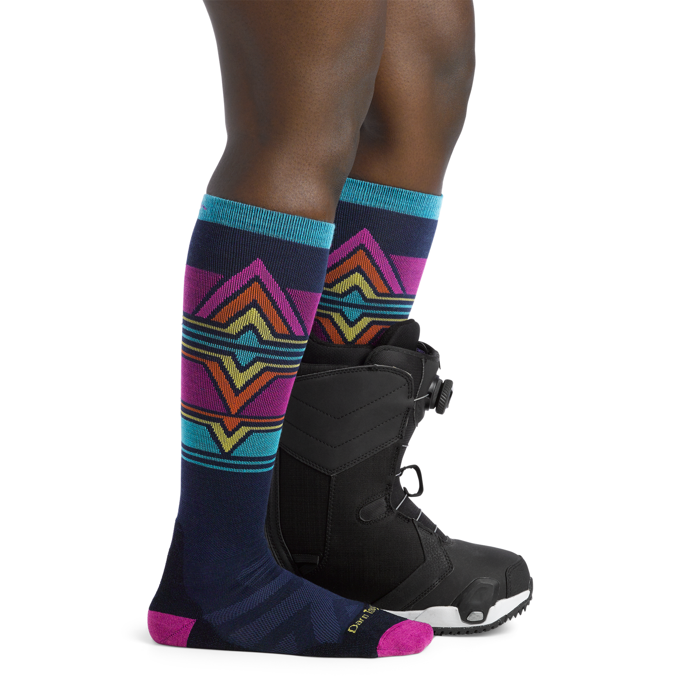 Woman facing to the right, wearing Echo Over the Calf Ski & Snowboard Socks in Eclipse, back foot also wearing a snowboard boot.