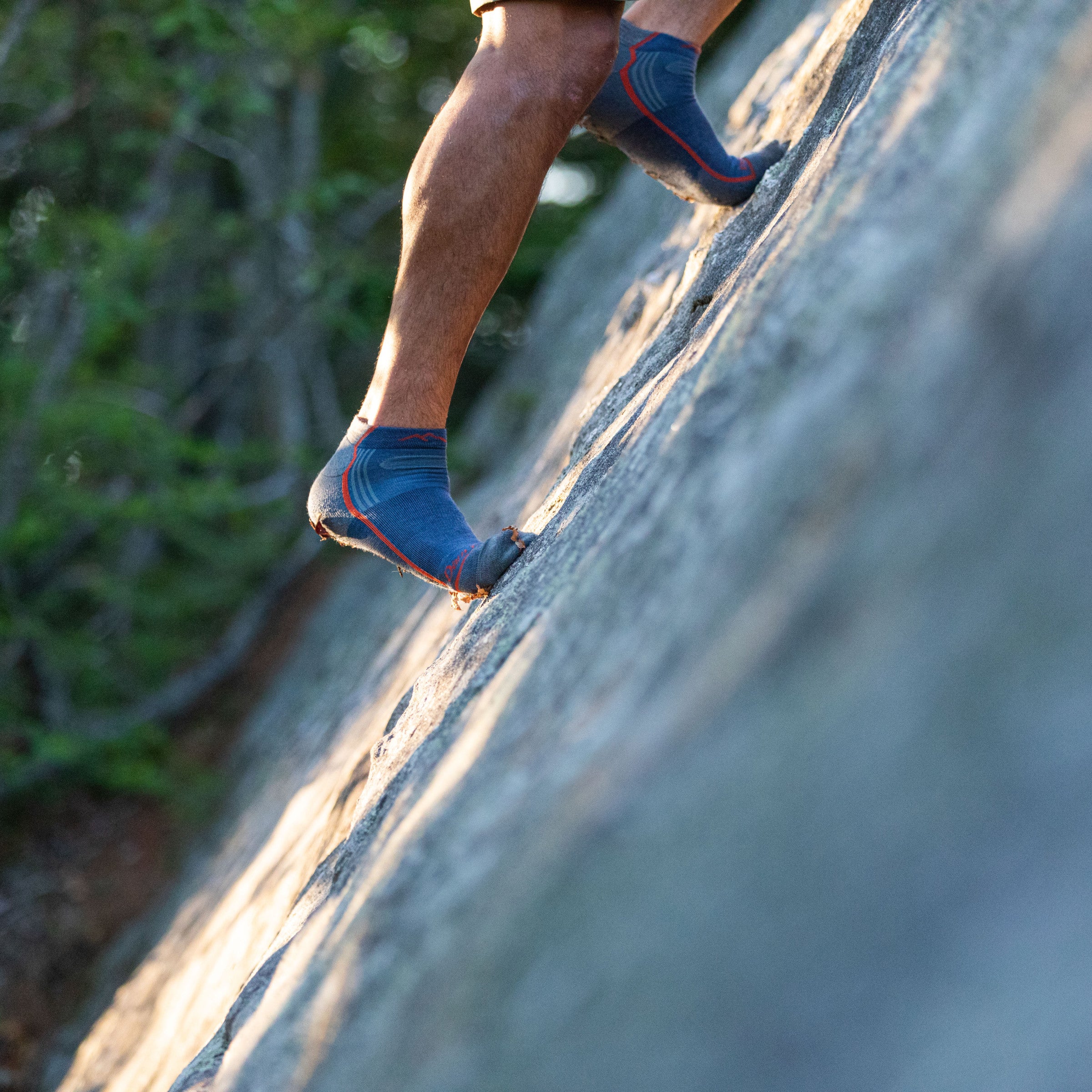 Side shot of model scaling a mountain wearing the men's light quarter hiking socks in denim with no shoes on