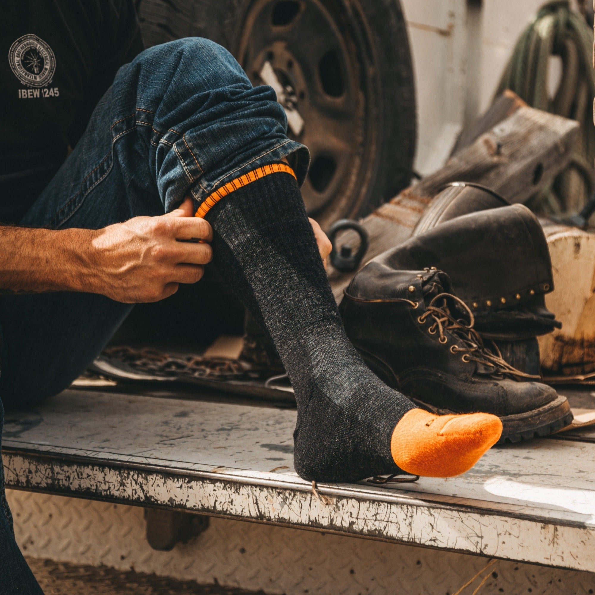 Model sitting on a work bench wearing men's 2006 steely boot work sock in graphite
