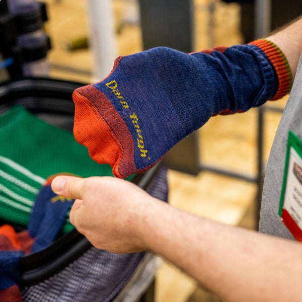 Hand holding a freshly knit pair of socks with the Darn Tough name on them