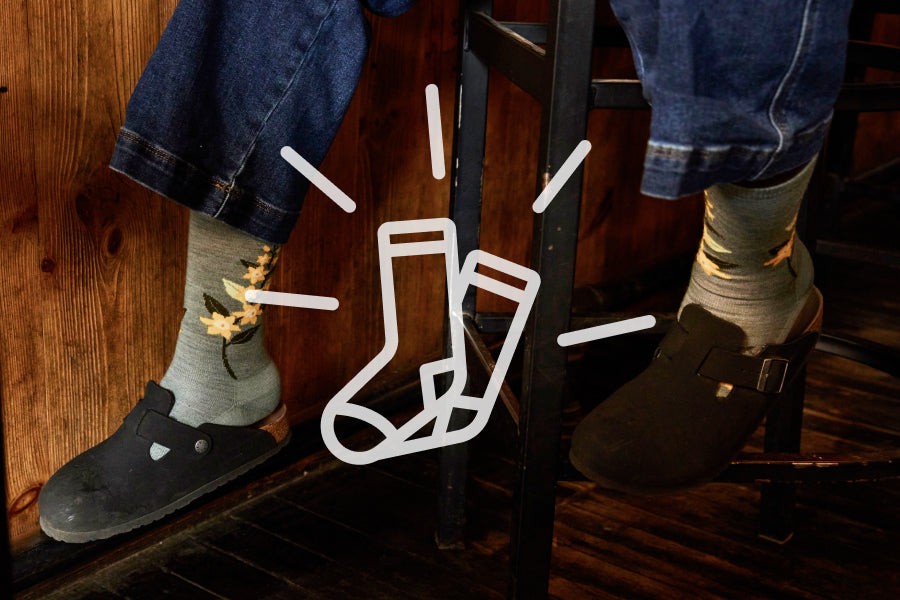 Feet on wearing red Darn Tough socks on green patterned rug with comfort sock graphic overlaid on image