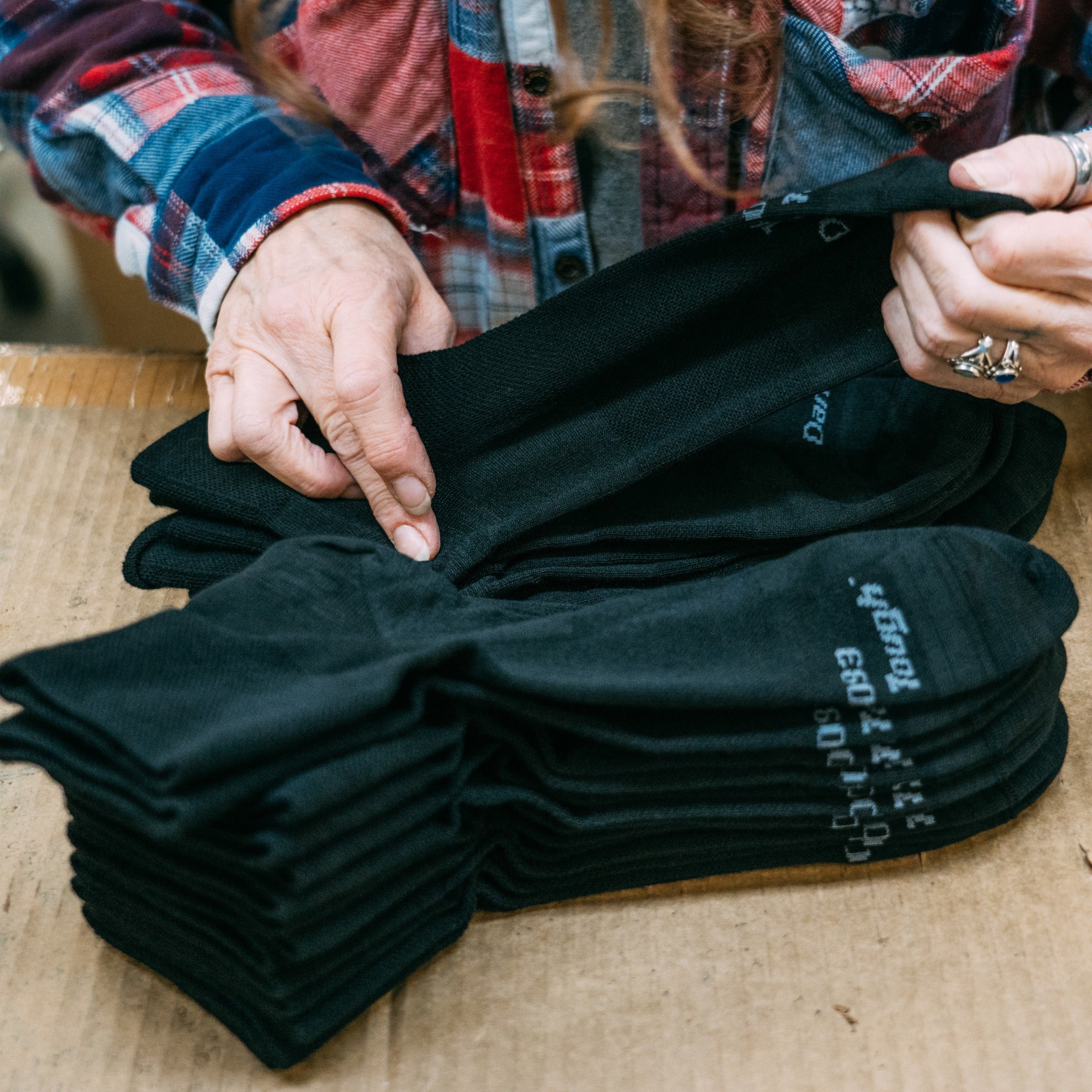 A stack of black quarter socks being folded by a Darn Tough employee