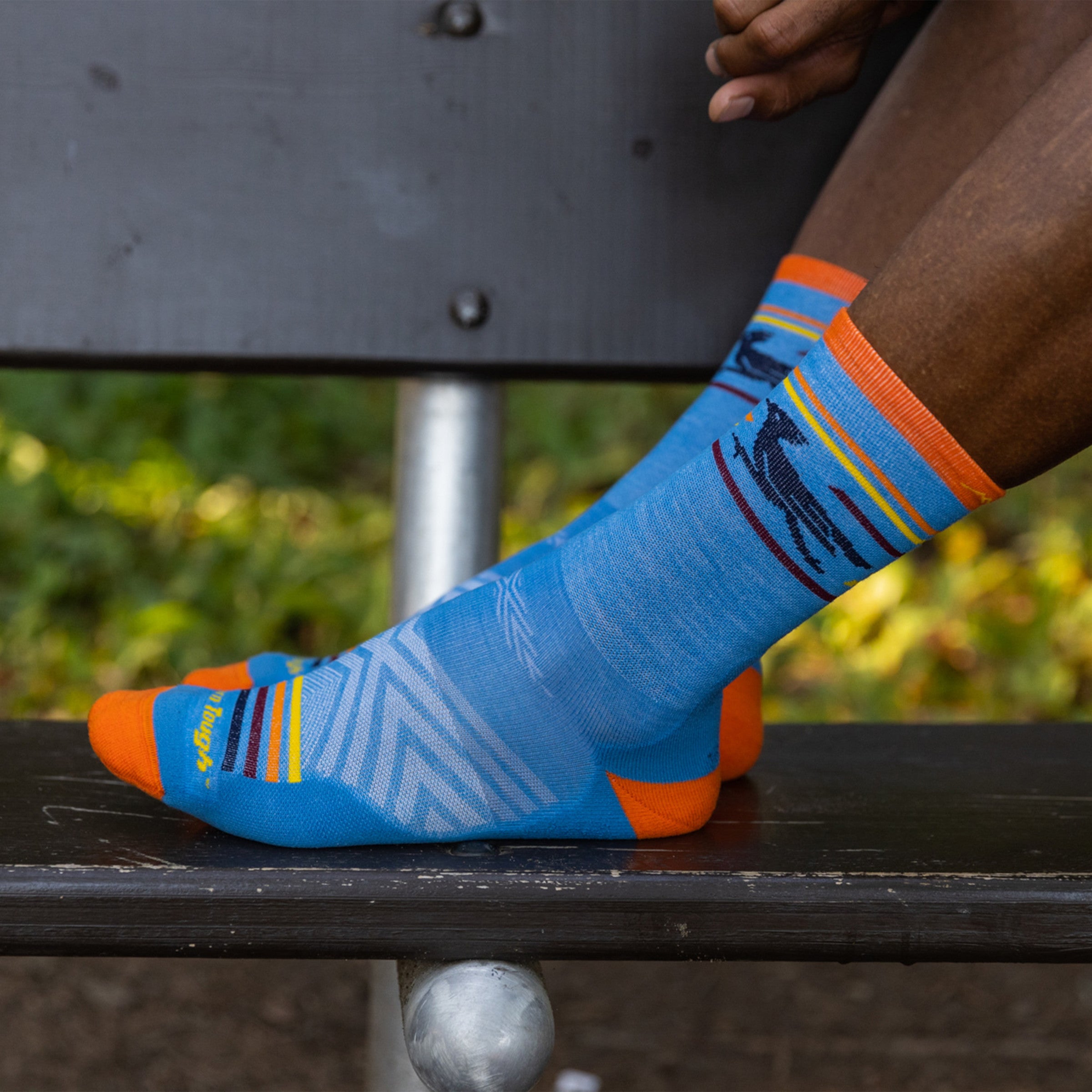 Side shot of model with their feet up on a bench wearing the men's frontrunner micro crew running socks in surf blue