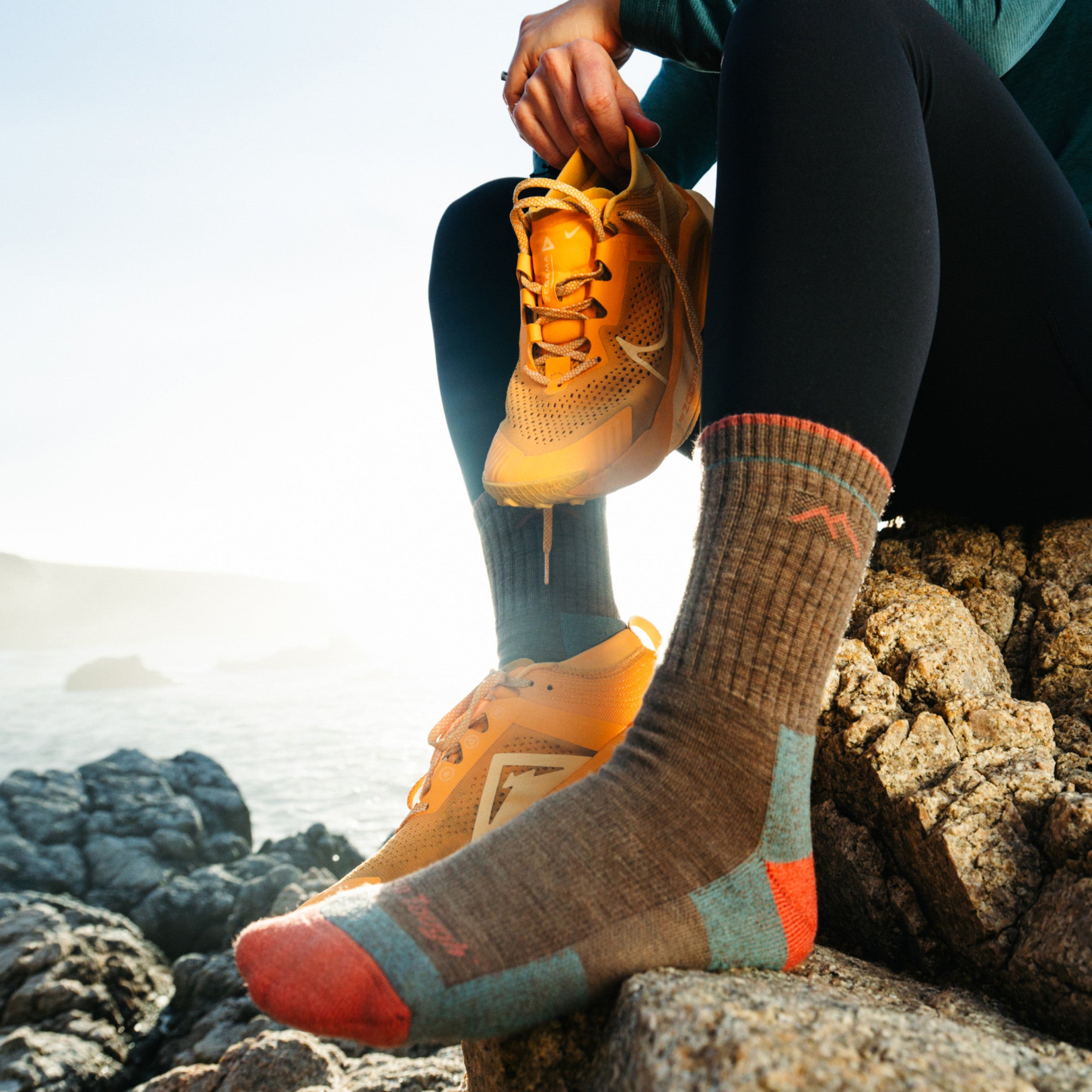 Model sitting on rock with one shoe off featuring the 1903 Midweight Hiker Micro Crew Hiking Sock in Bark