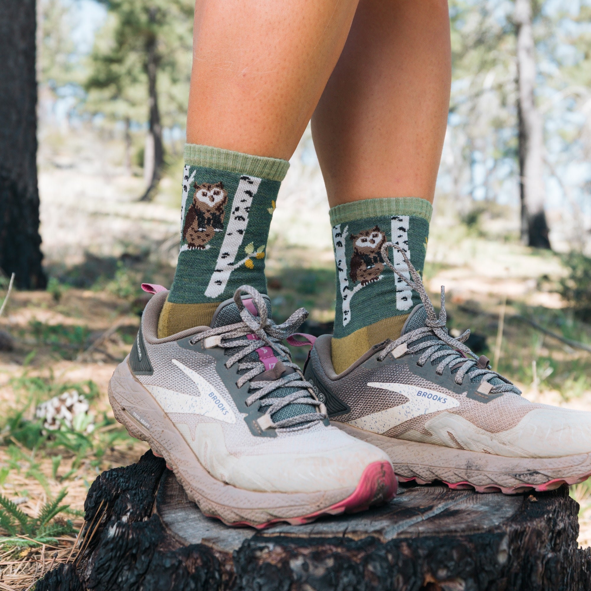 model standing on stump in sneakers wearing the 5001 critter club micro crew hiking sock in owl green 