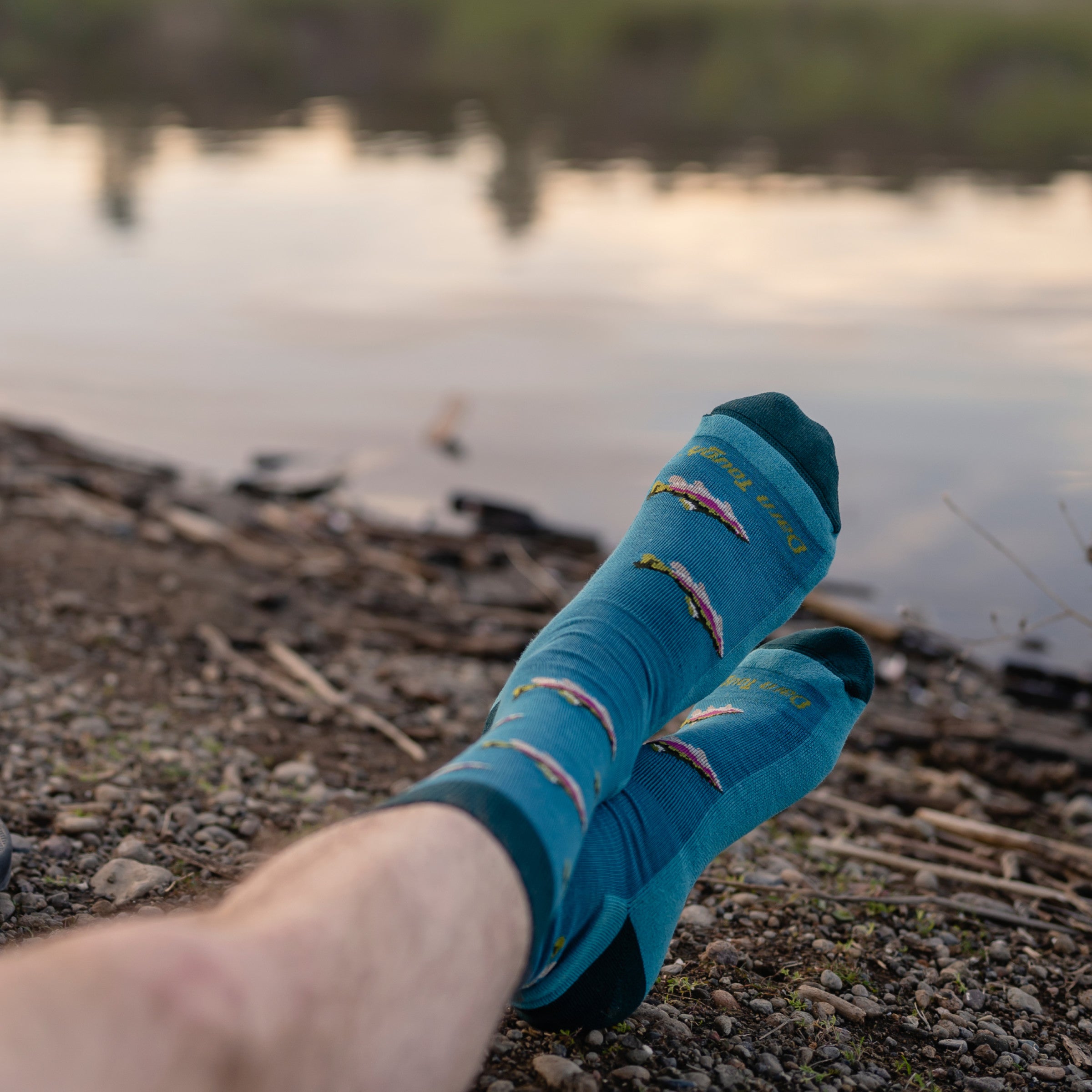 close up shot of a model sitting on a rocky beach with legs crossed wearing 6085 socks in cascade blue colorway without shoes