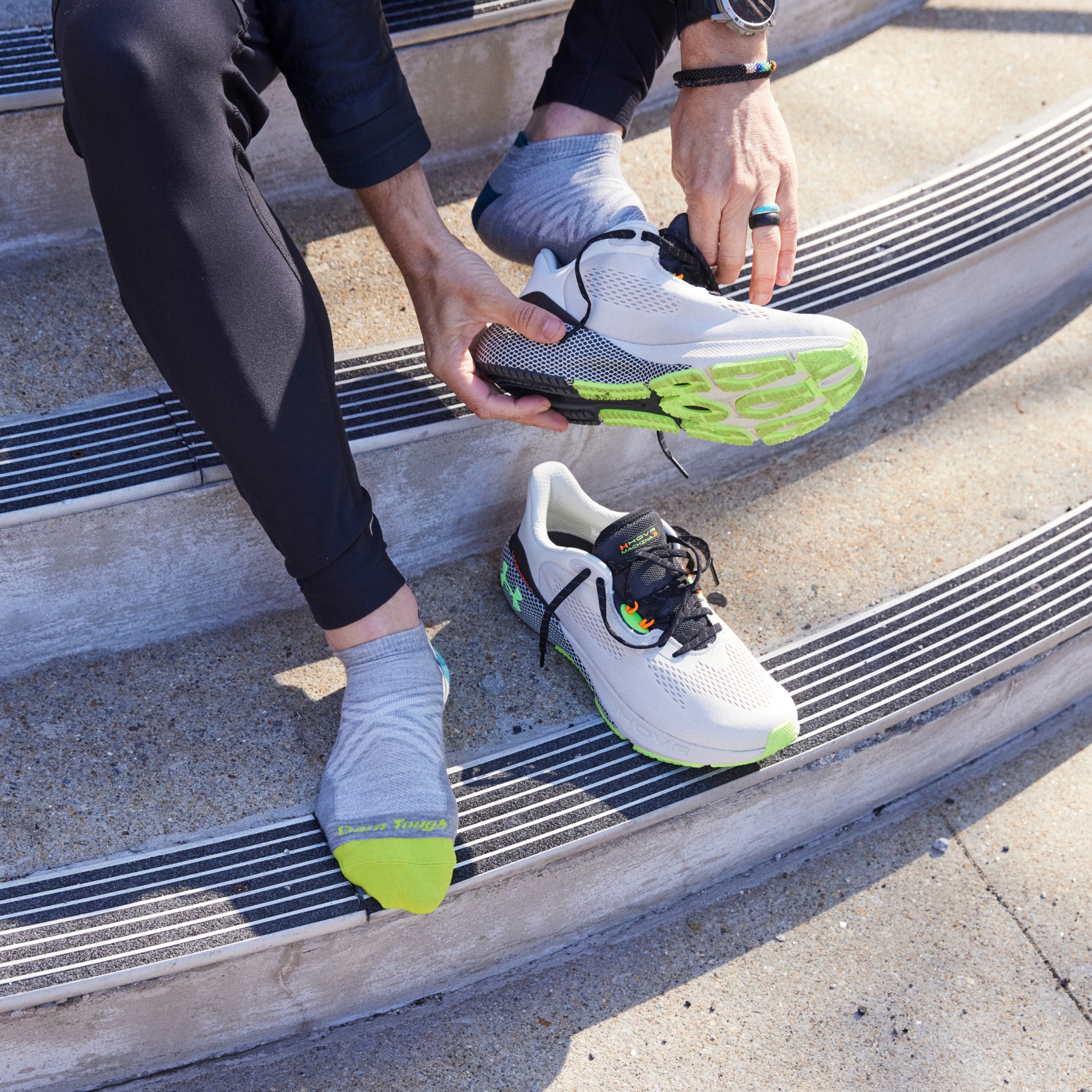 Model sitting on concrete steps wearing 1033 socks in Gray colorway while putting on white running shoes