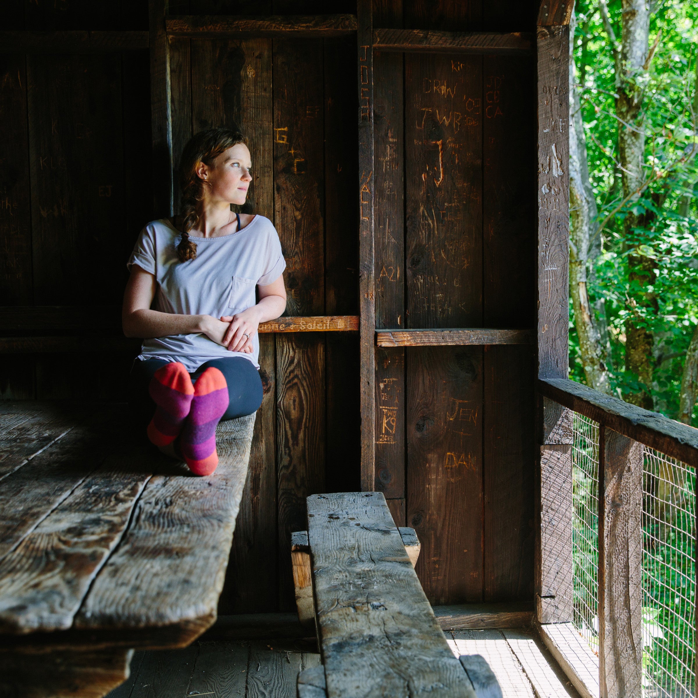 A woman sitting on a wooden picnic table wearing a t-shirt, leggings and Women's Hiker Quarter Hiking Socks in Plum Heather