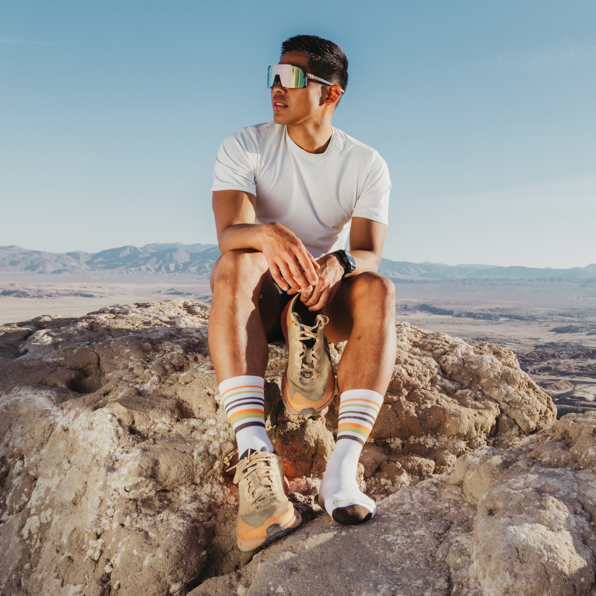 model sitting on the mountain top holding one shoe wearing the 5012 fast pack lightweight micro crew hiking sock in white colorway