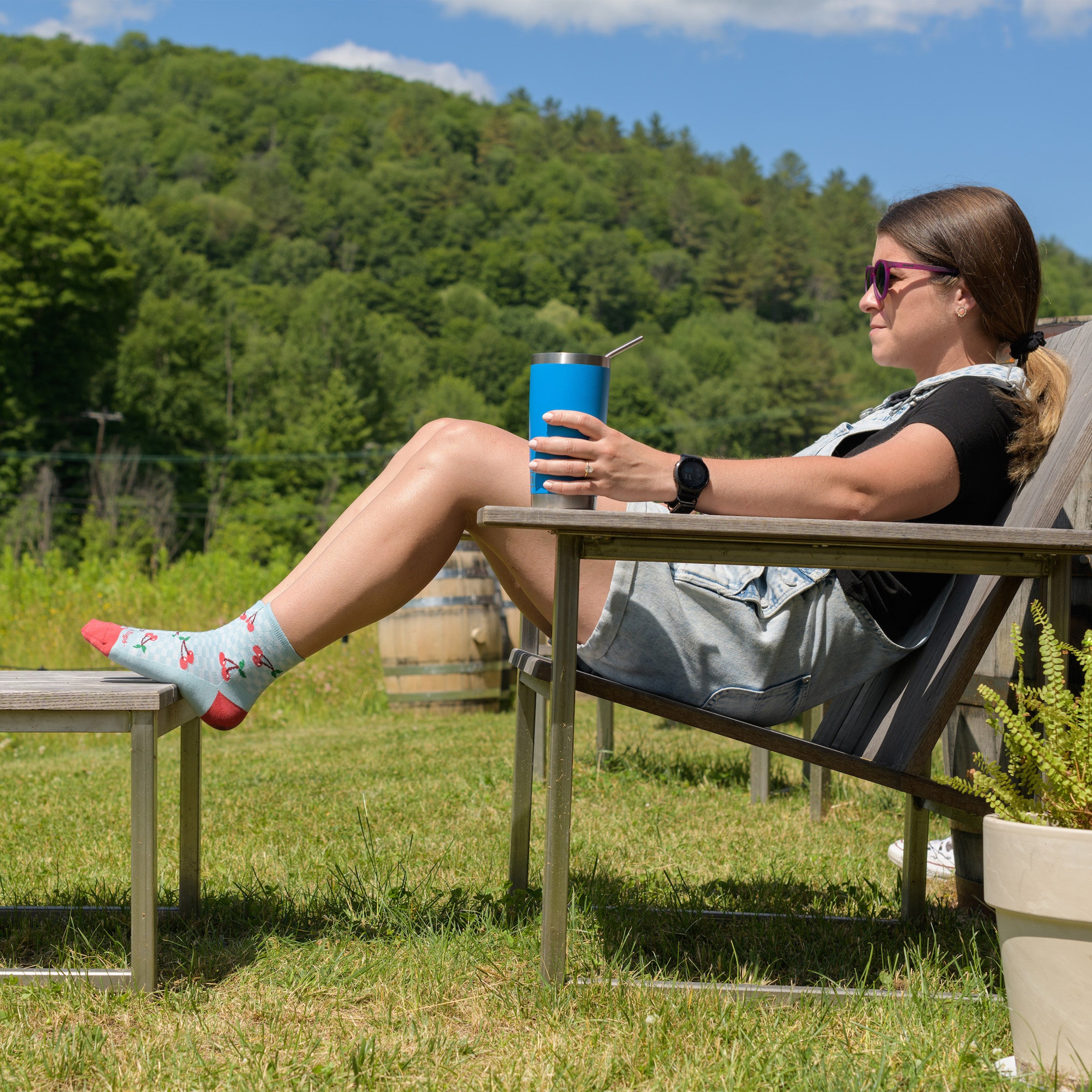 Full shot of model sitting in a chair outside wearing the women's fruit stand shorty lfiestyle socks in glacier blue