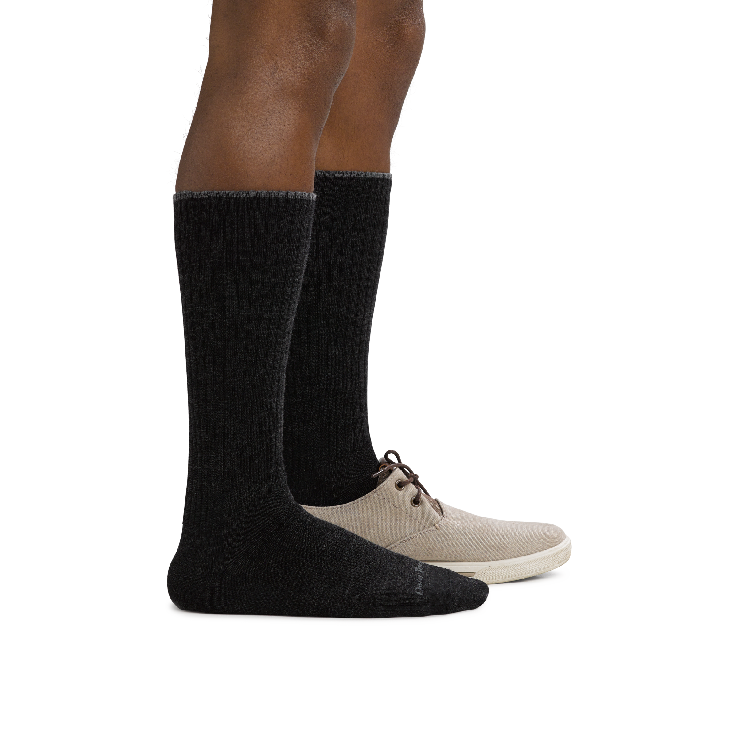 Man standing facing to the right wearing The Standard Mid-Calf Lightweight Lifestyle Sock in Black, with back foot in a shoe as well