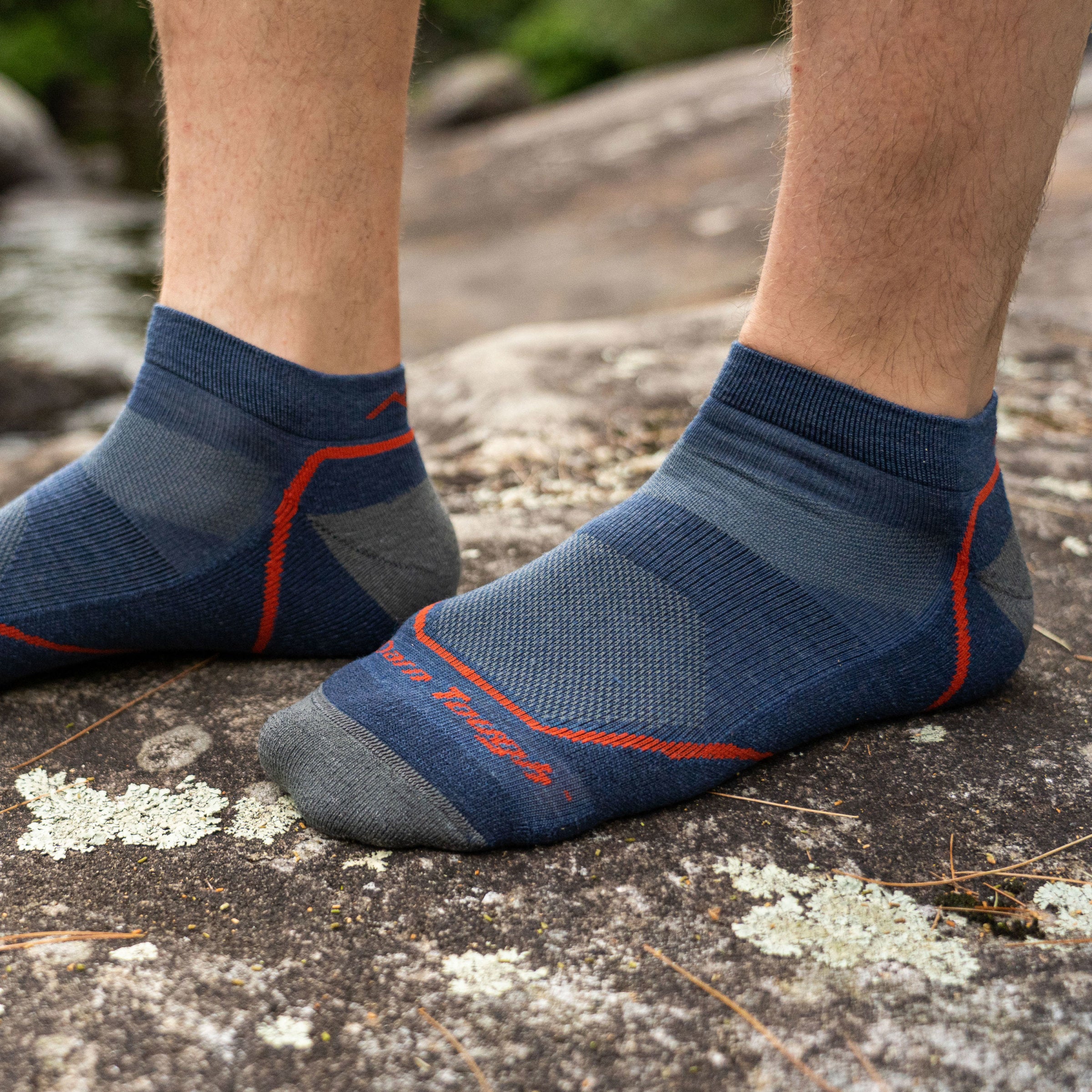 Close up of a man's feet, standing on a rock wearing only Light Hiker No Show Lightweight Hiking socks in Denim