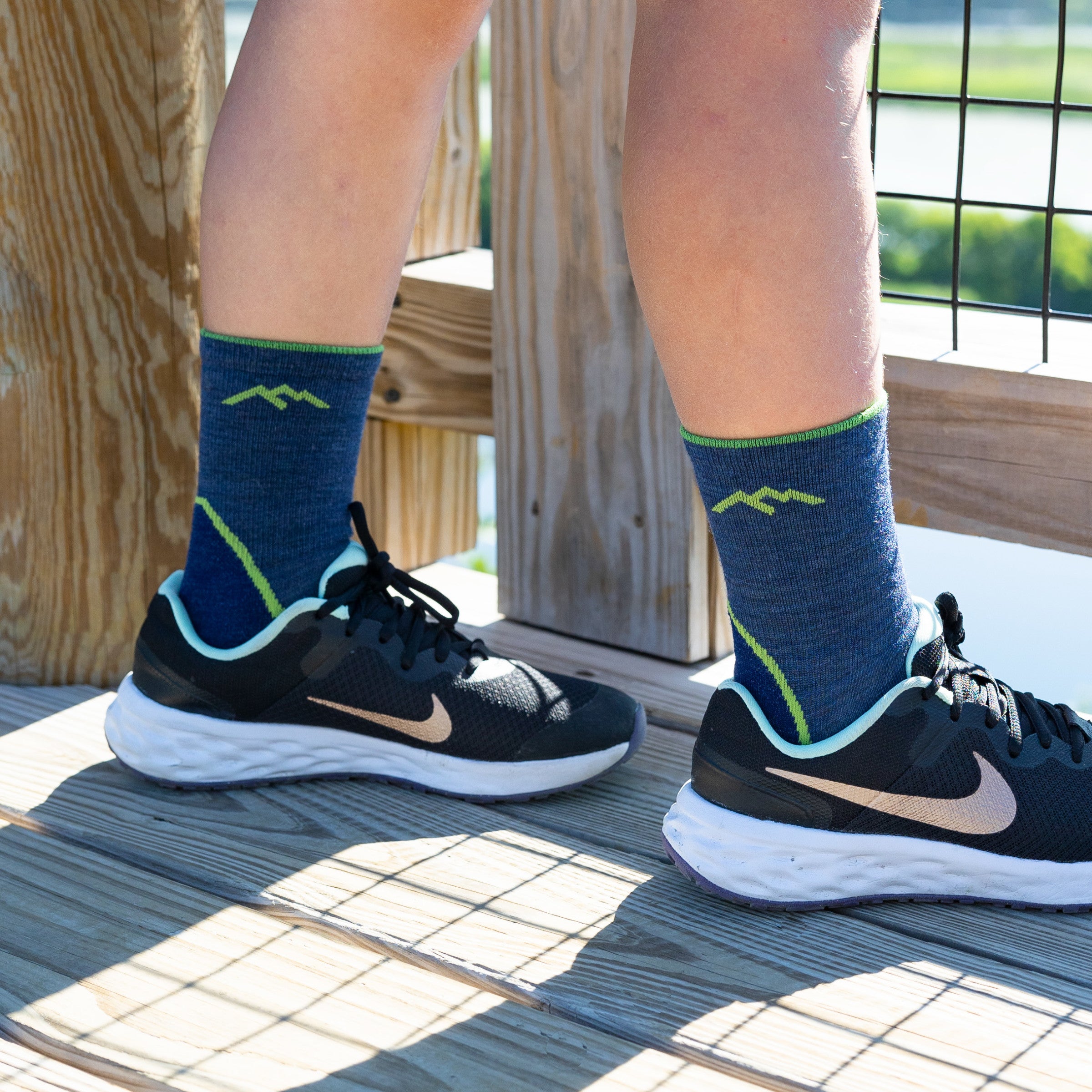 Close up shot of kid wearing light hiker socks in denim, standing on wooden nature overlook.