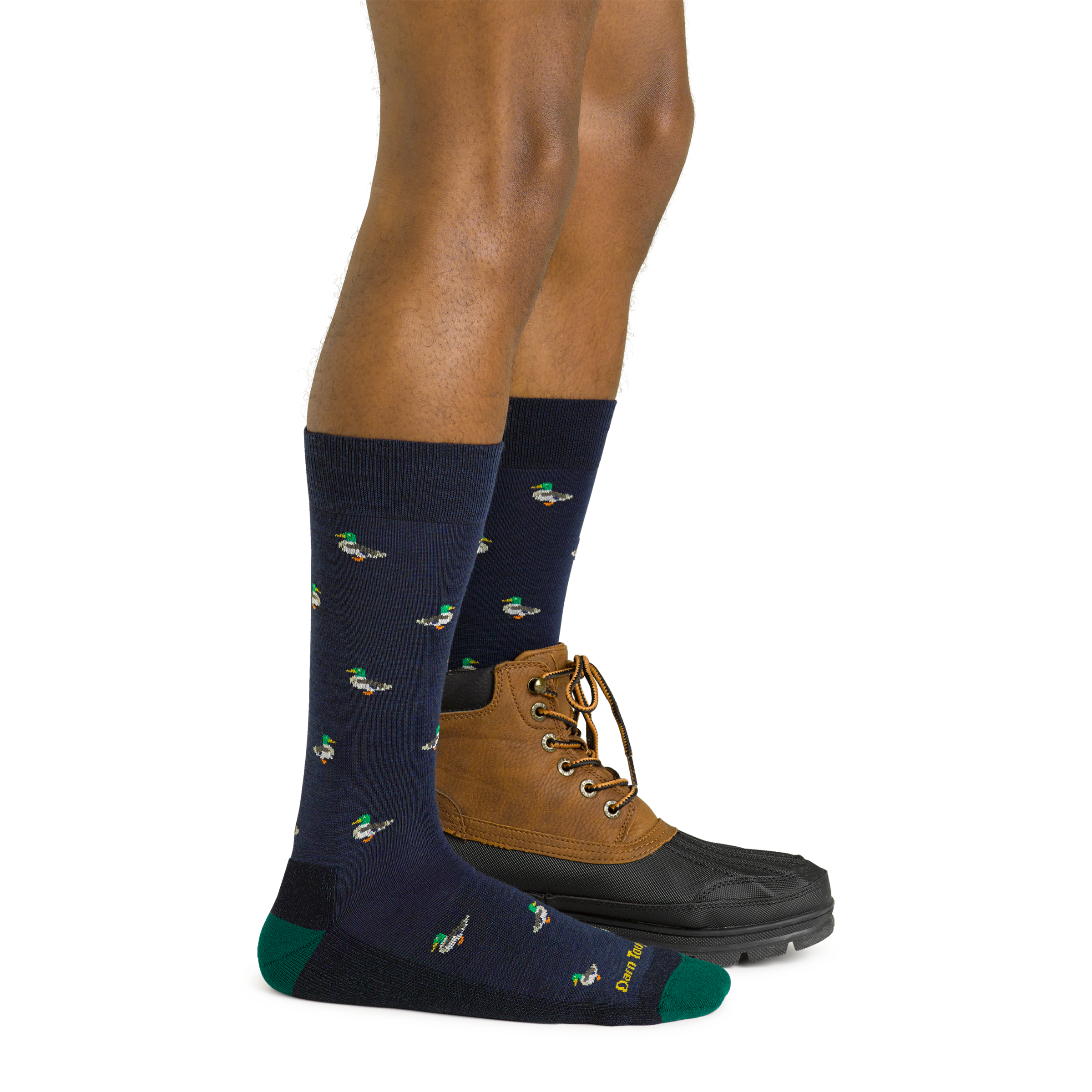 Side studio shot of model wearing men's duck duck moose crew lifestyle sock in navy eclipse with brown boot on left foot