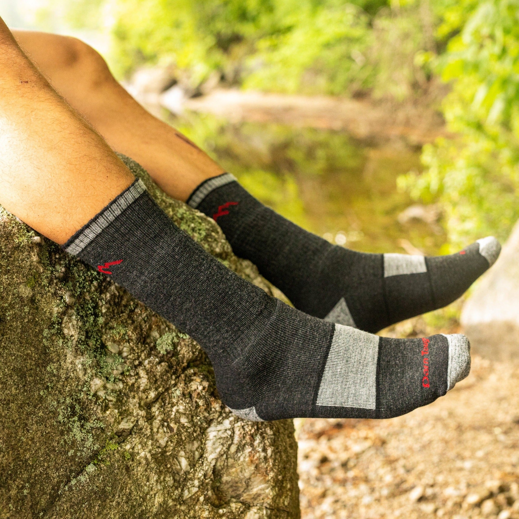 Side shot of model sitting on river rocks wearing the men's micro crew hiking sock in black with brown hiking shoes on