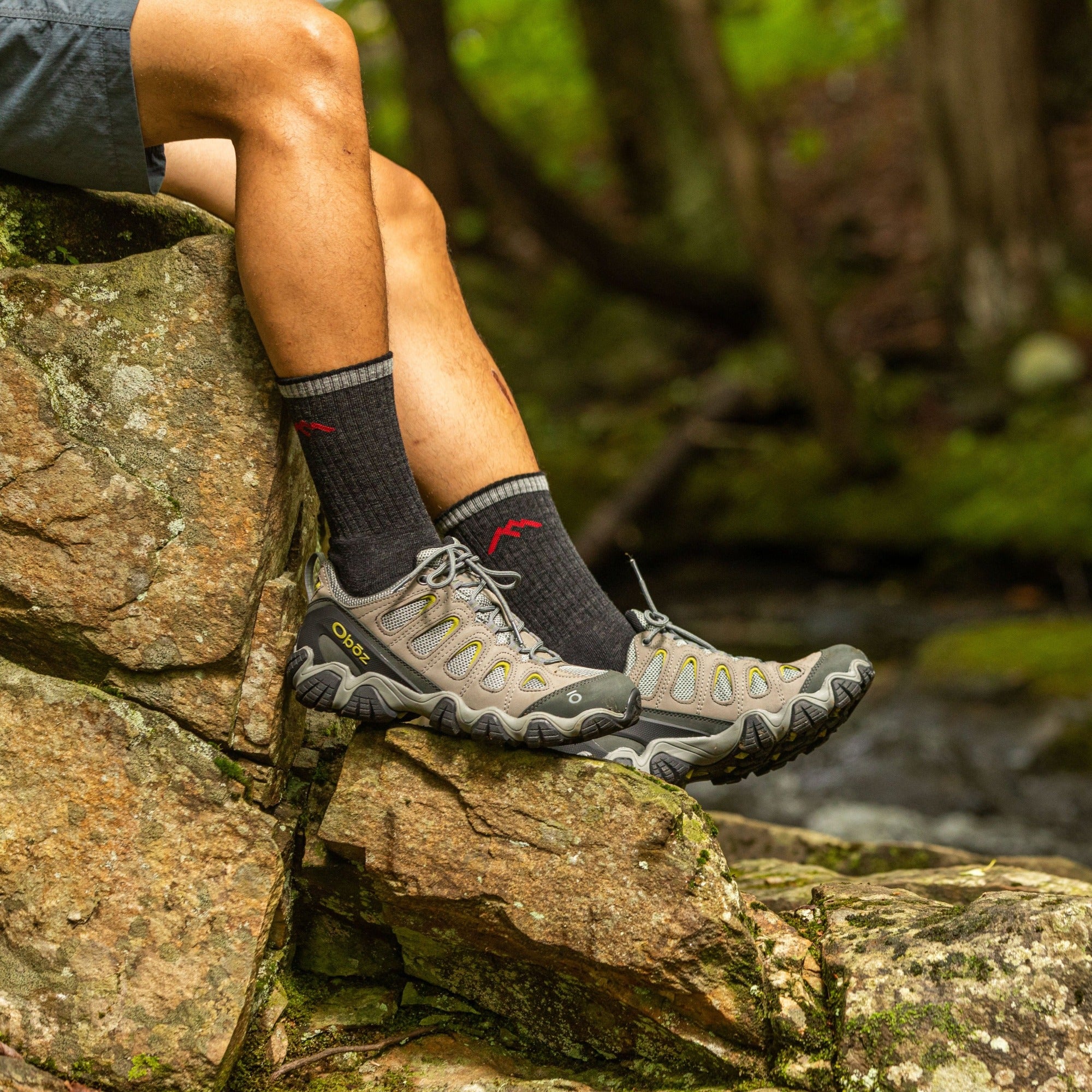 Close up shot of model sitting on a rock wearing the men's boot hiking sock in black
