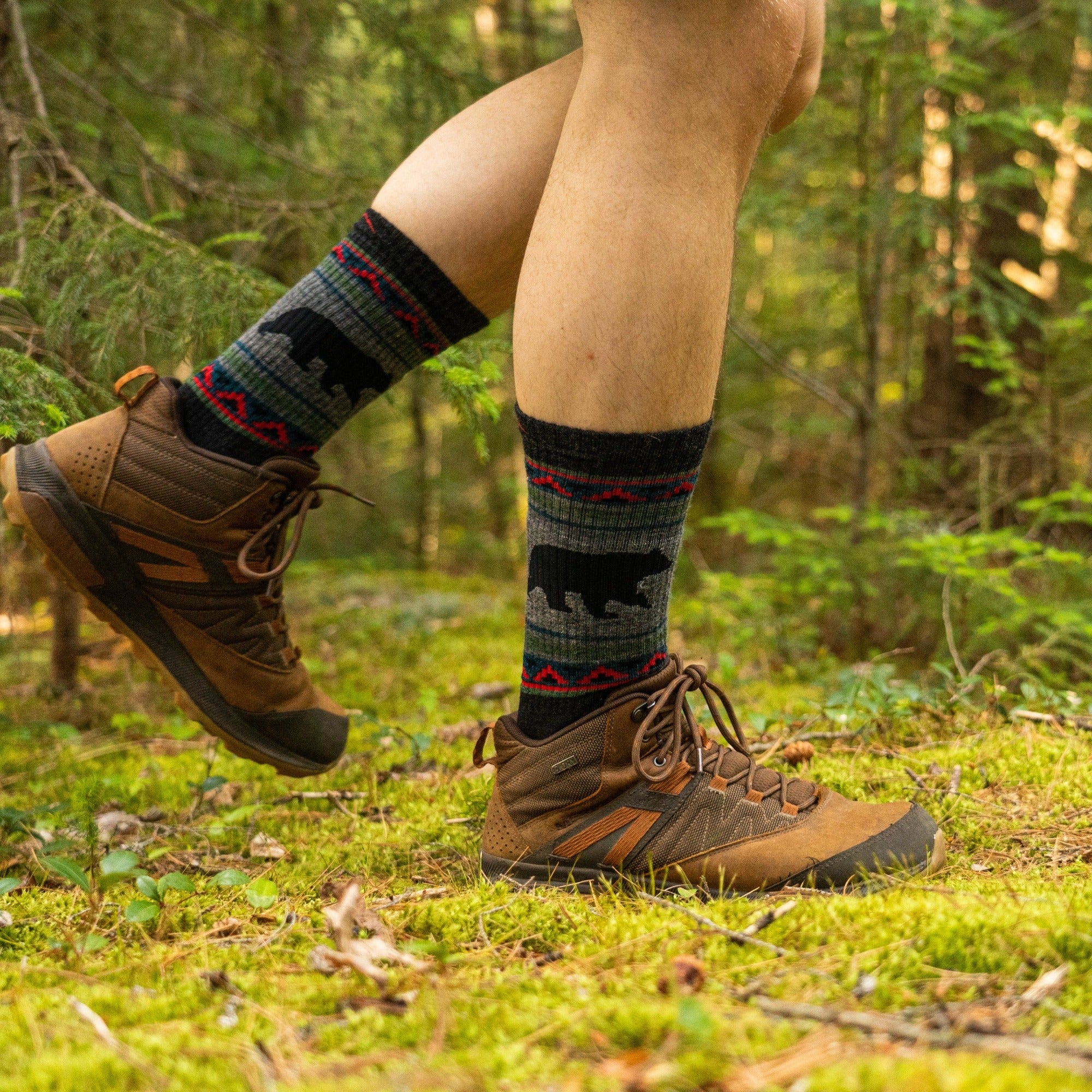 Close up lifestyle image of a man walking on a mossy trail in a forest, wearing hiking boots and VanGrizzle Boot Midweight Hiking Sock in Charcoal