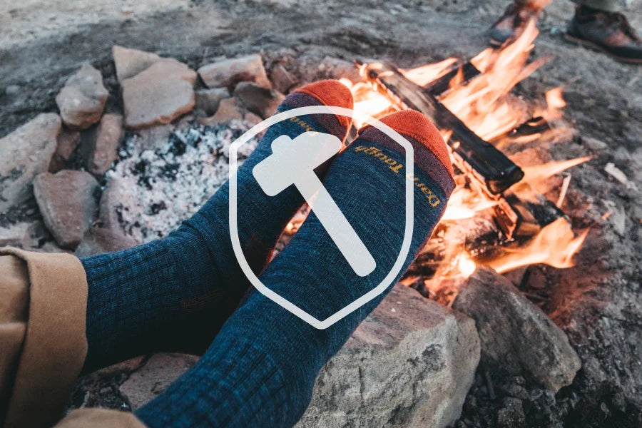 Feet wearing durable hiking socks by a fire with a durability hammer symbol overlaid