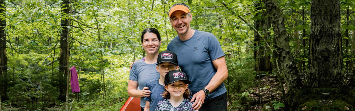 A couple with two young children out for a family hike, the kids both sporting Darn Tough baseball caps