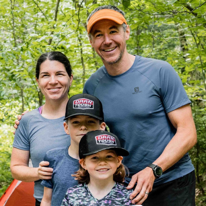 A couple with two young children out for a family hike, the kids both sporting Darn Tough baseball caps