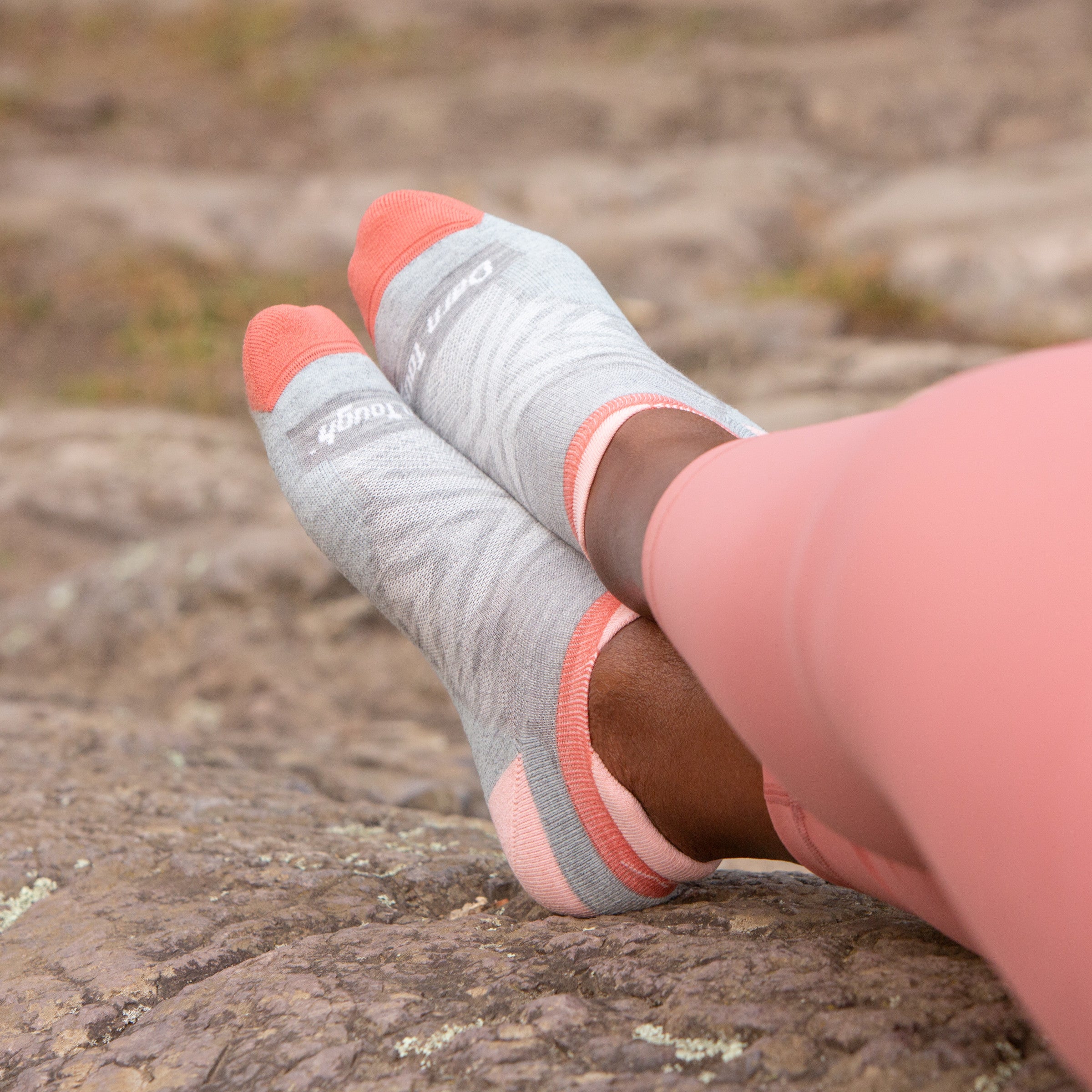 Close up lifestyle shot of model wearing no show tab socks in Ash, paired with coral-colored leggings.