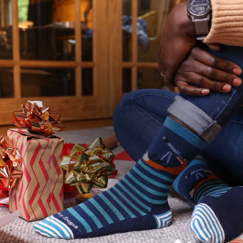 Feet wearing Darn Tough socks next to piles of bows and wrapping paper