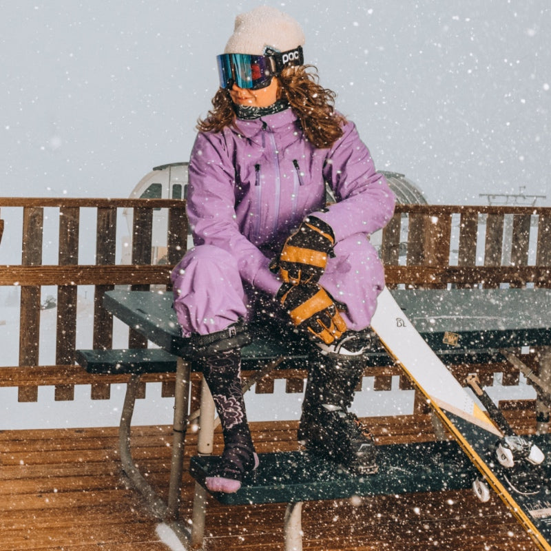 A skier and snowboarder at a top-of-the-mountain lodge on a snowy day in Darn Tough socks