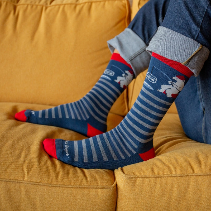 Feet on a couch wearing blue striped merino wool socks with an ice fishing polar bear design