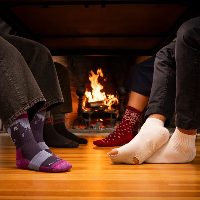 Feet seated below a table at a holiday meal, 3 pairs looking good in Darn Tough, one wearing holey socks