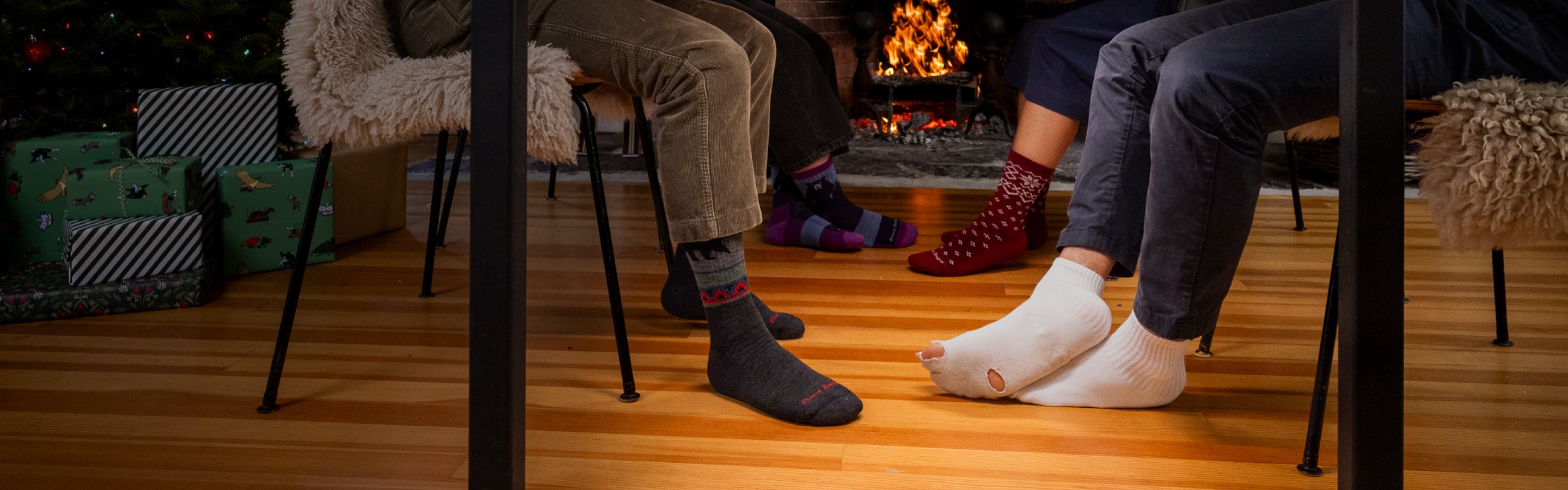 Feet seated below a table at a holiday meal, 3 pairs looking good in Darn Tough, one wearing holey socks